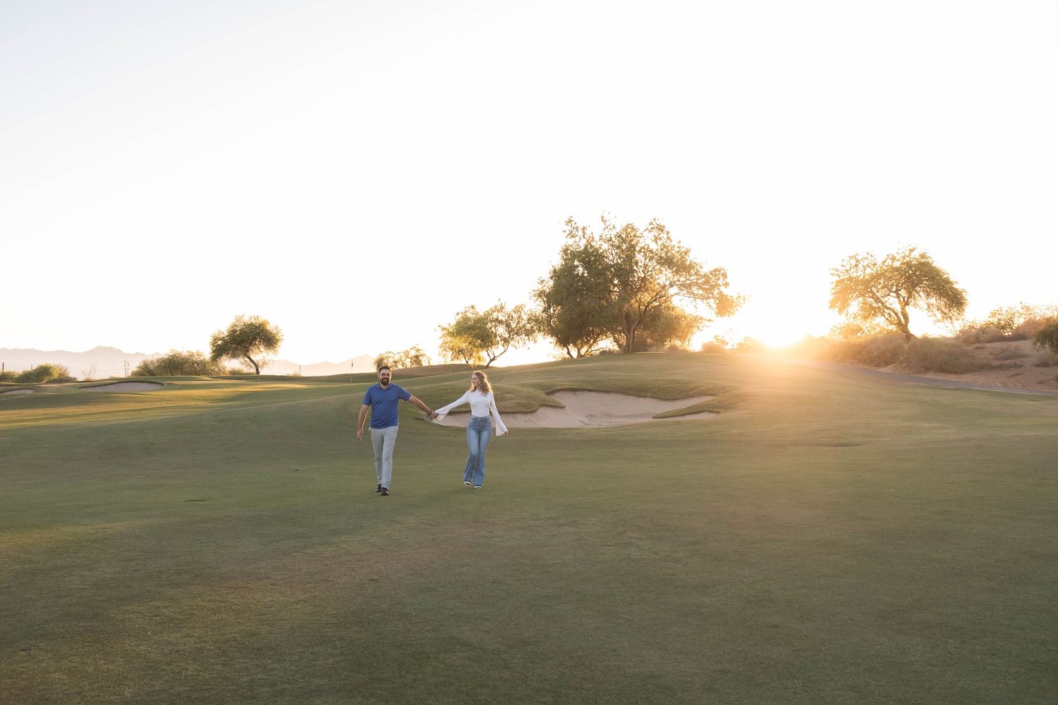 Two people walking hand in hand on a golf course at sunset.