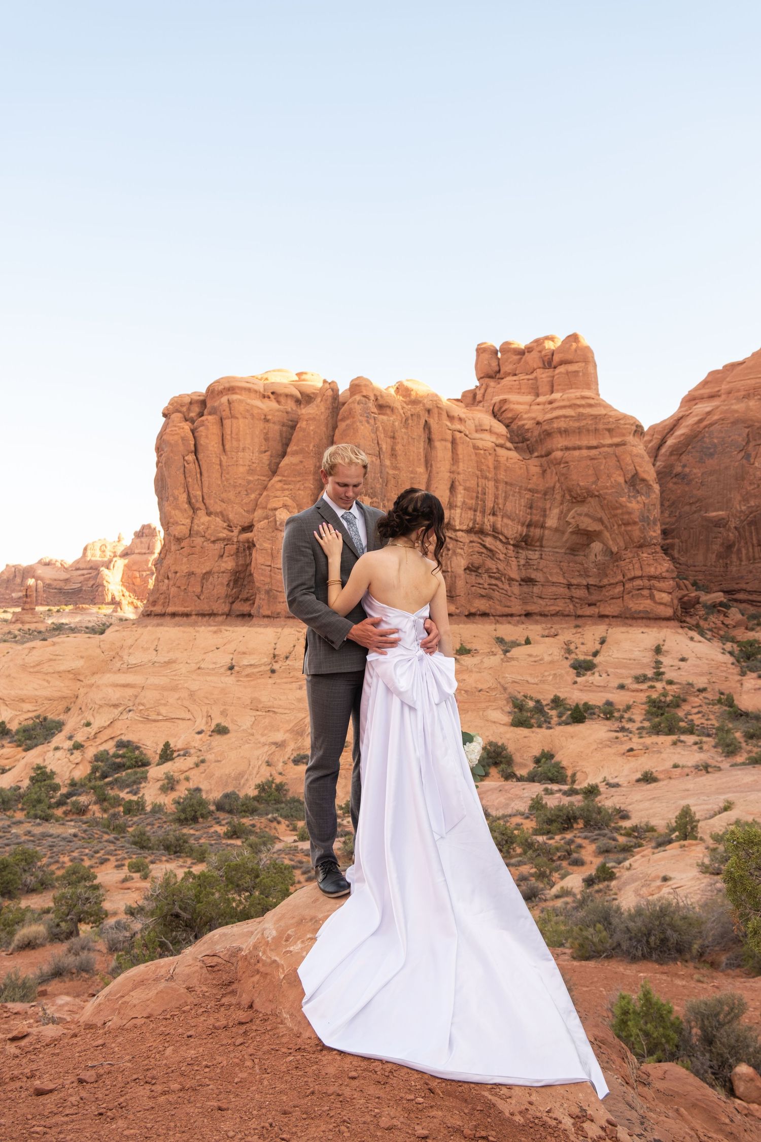 A couple embraces against the stunning backdrop of red rock formations in Arches National Park at sunset.