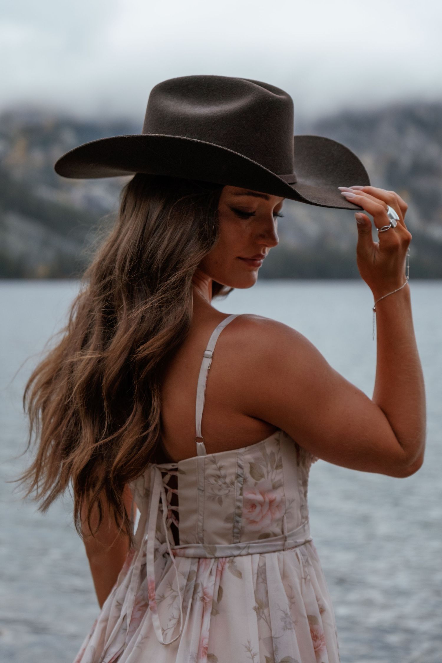 A woman in a flowy white sundress and wide-brimmed hat poses by the water in a series of artistic shots.