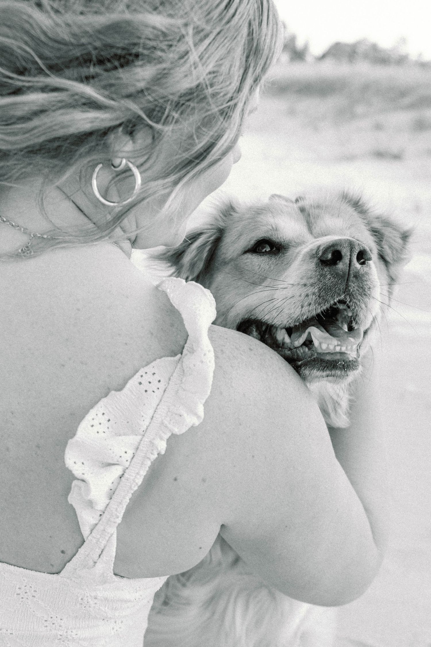 A happy dog rests its head on someone's shoulder wearing a white dress in this black and white photograph.