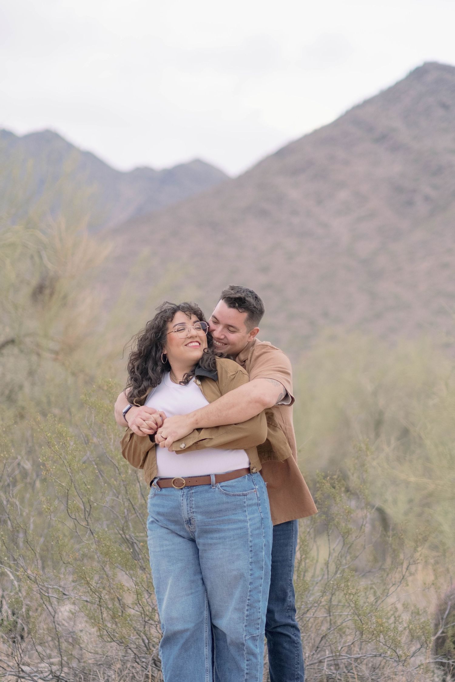 A couple shares a tender moment against a backdrop of desert mountains.