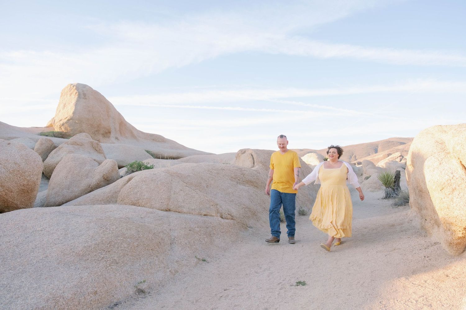 Couple walking through desert terrain at sunset holding hands.