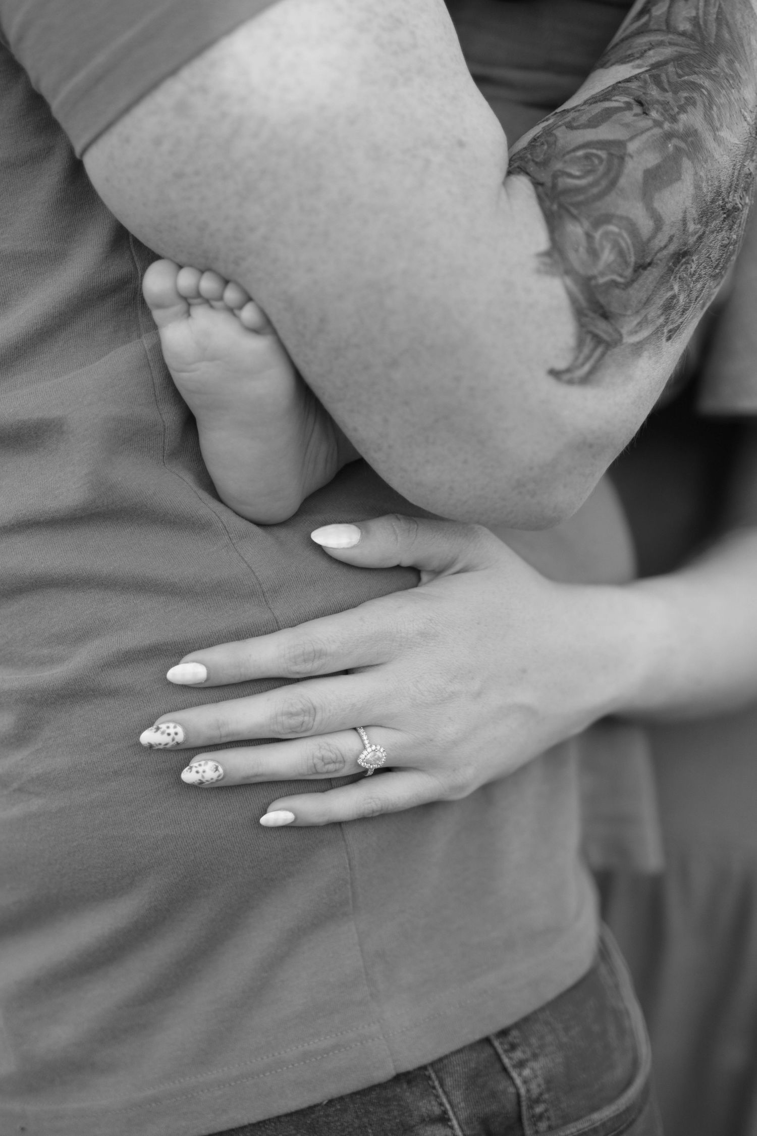 Close-up of hands and baby feet showing wedding ring details in black and white.