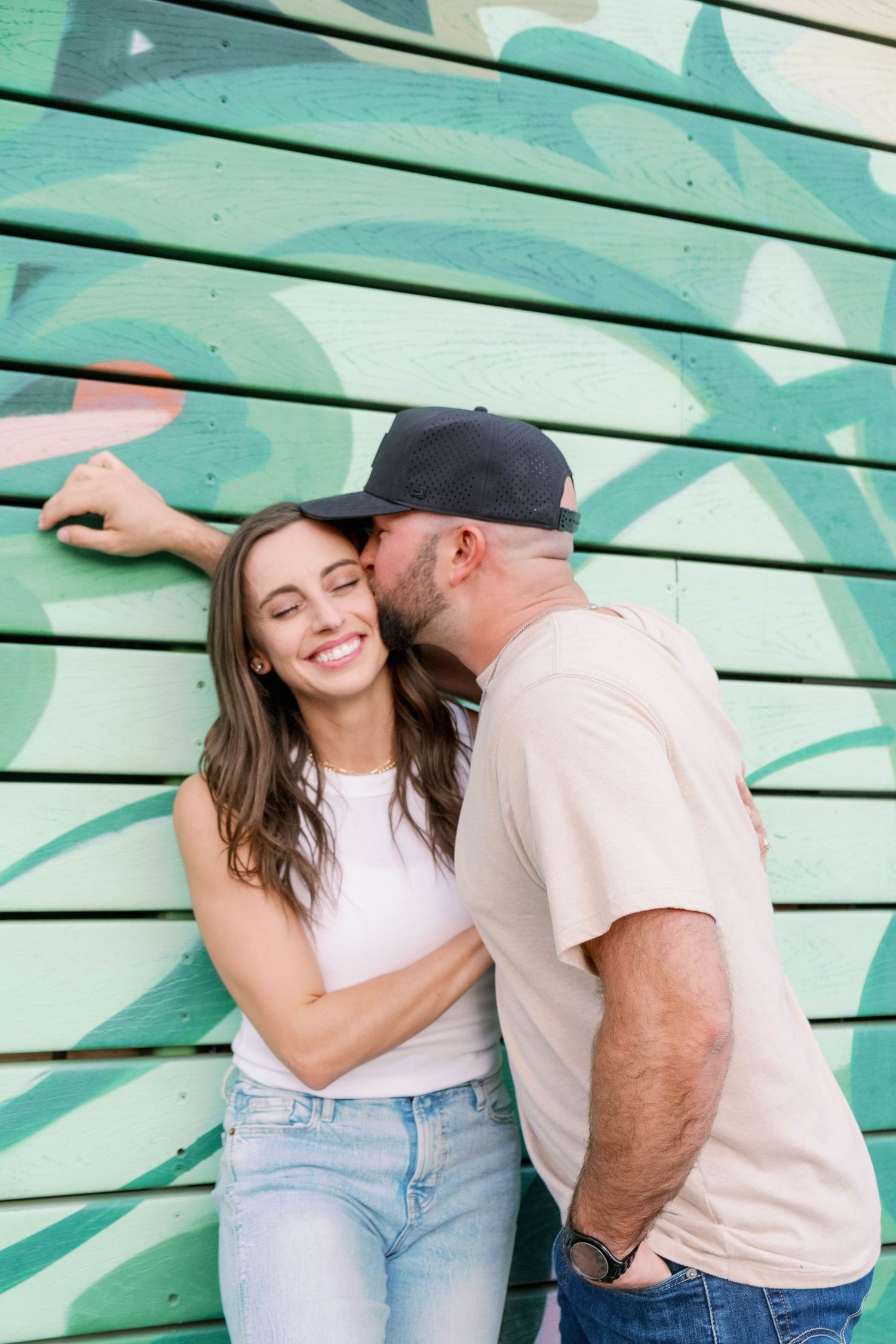 Playful couple posing against a mural wall in casual attire.