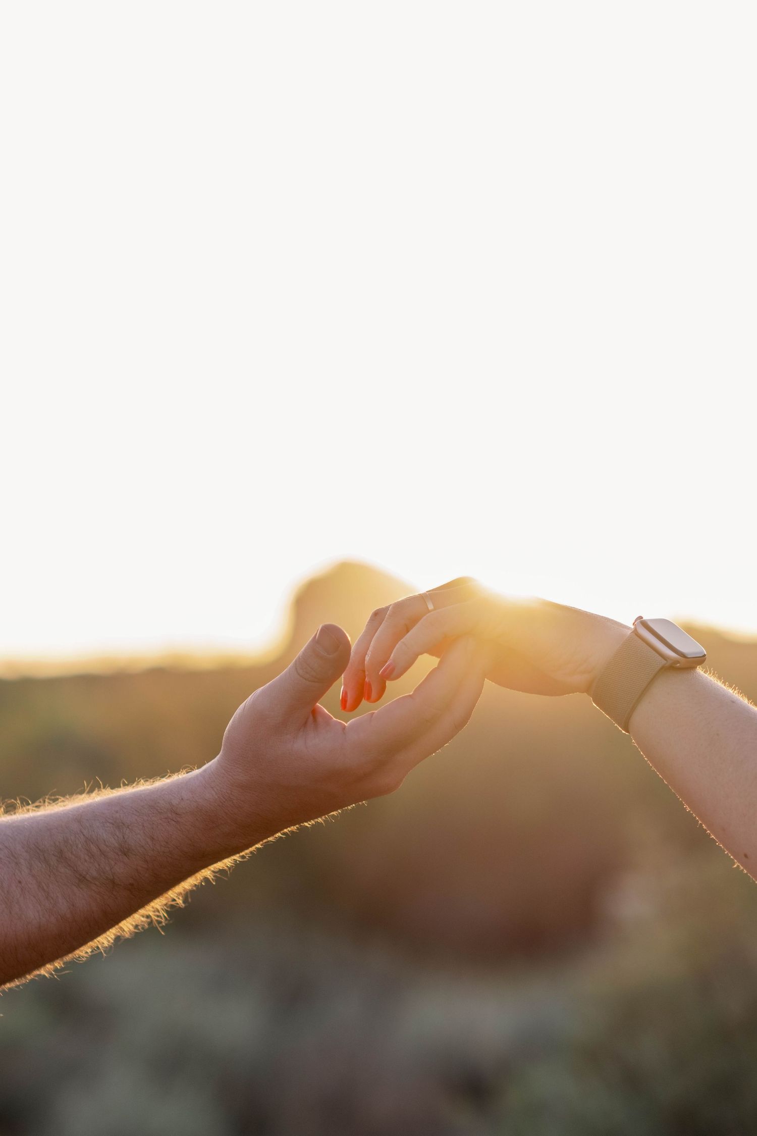 Close-up silhouette of hands touching during sunset engagement photo session.