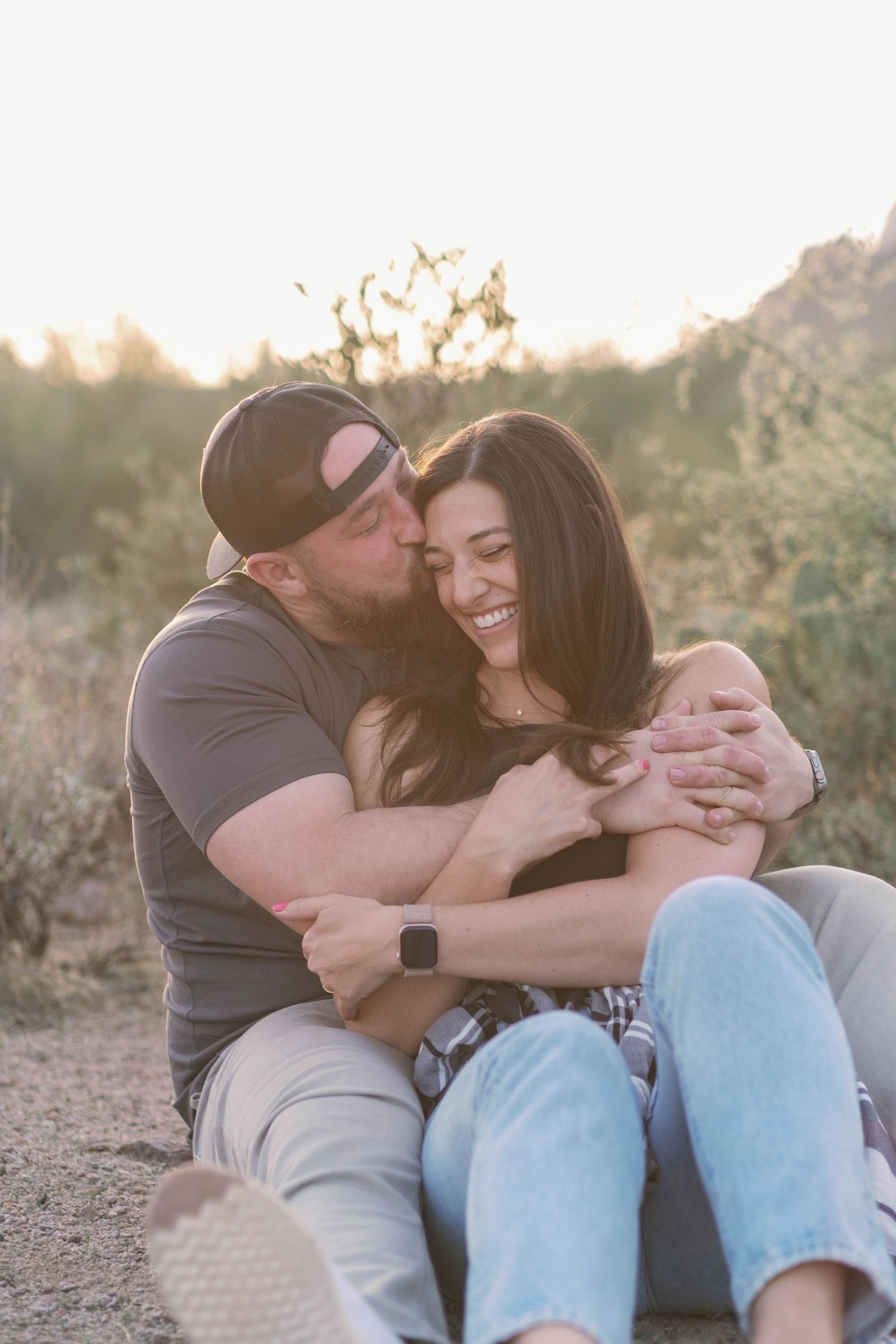 Tender moments captured between two people sitting in desert terrain at sunset.