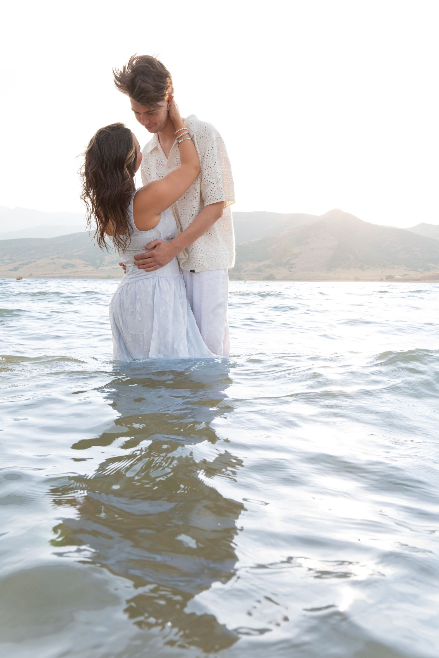 A couple embraces while wading in ocean waves during a romantic beach photoshoot at sunset.