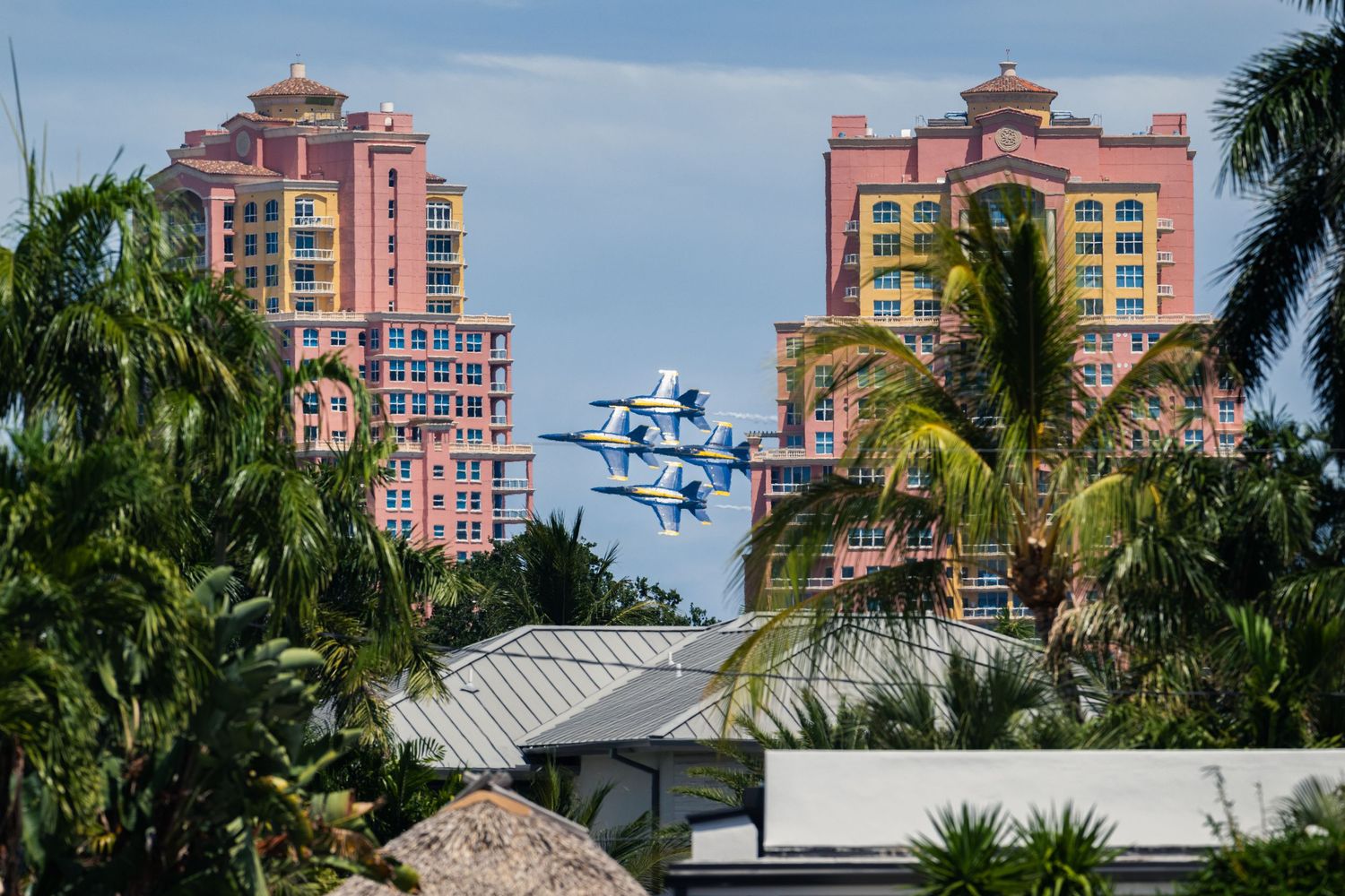 Blue Angels jets fly between The Palms Condominiums buildings and palm trees in Fort Lauderdale, capturing aerial precision.