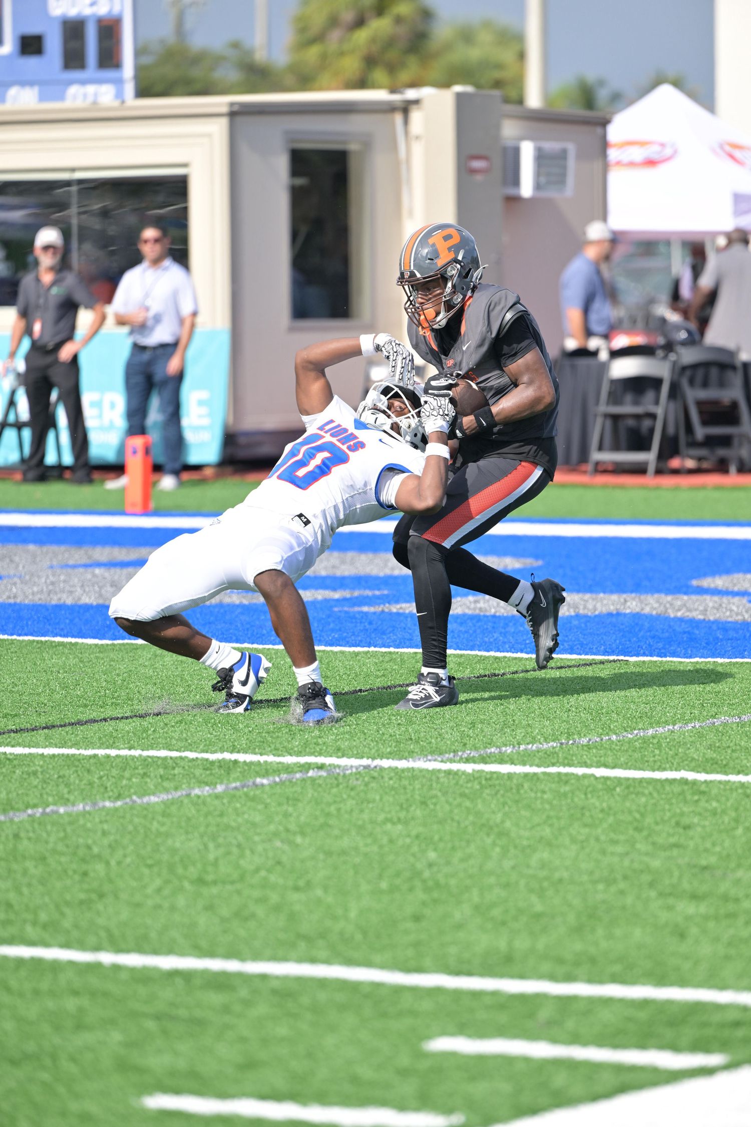 Football player in black Bengals uniform catching ball while being tackled by blue jersey defender.