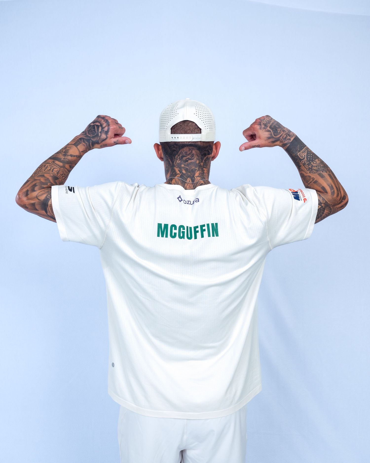 McGuffin athlete flexing biceps showing tattoos, wearing white jersey and cap, back view.