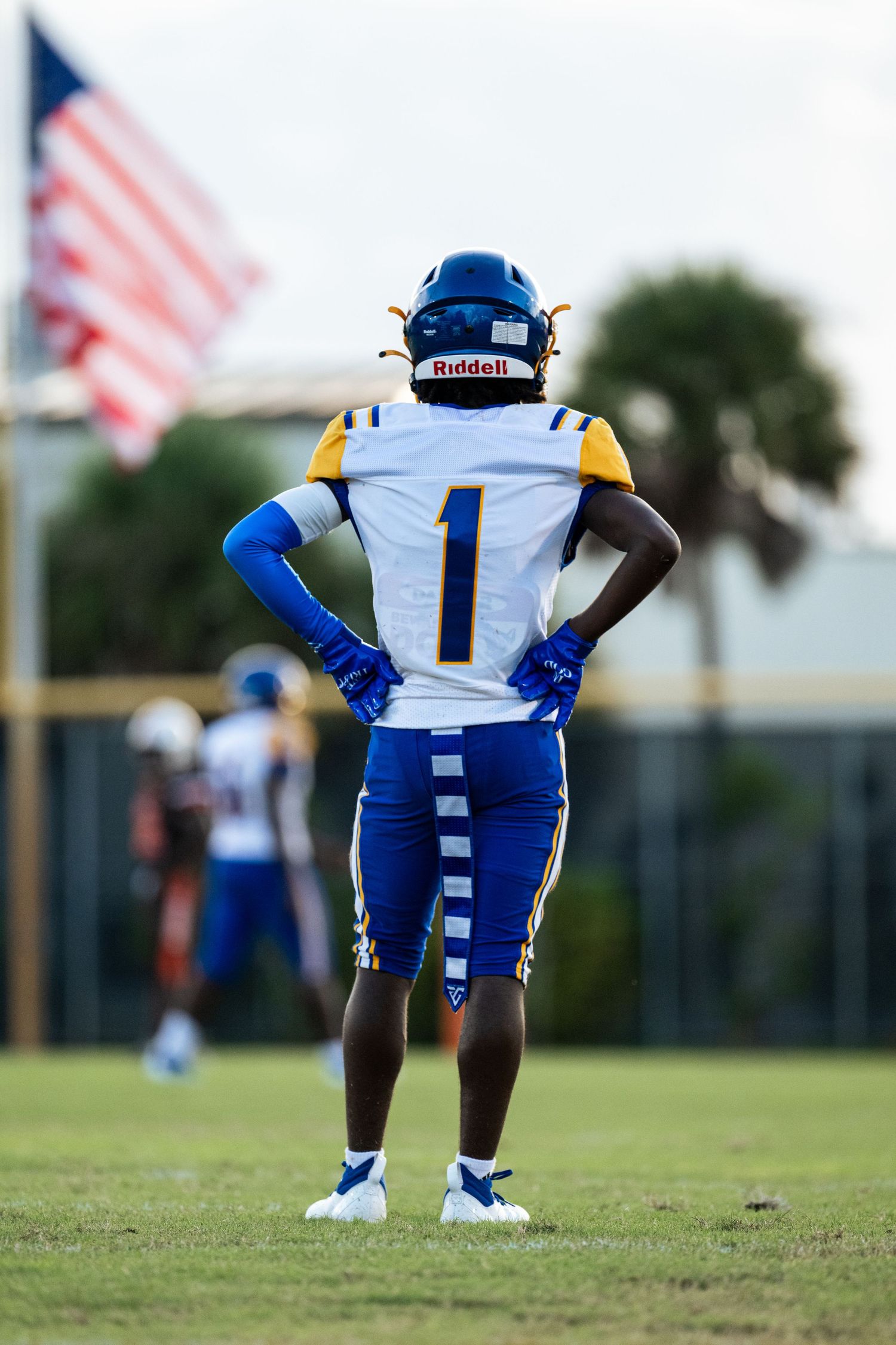 Athlete in blue and white football uniform stands on the field with aAmerican flag backdrop, symbolizing pride and readiness in Sunrise, FL.