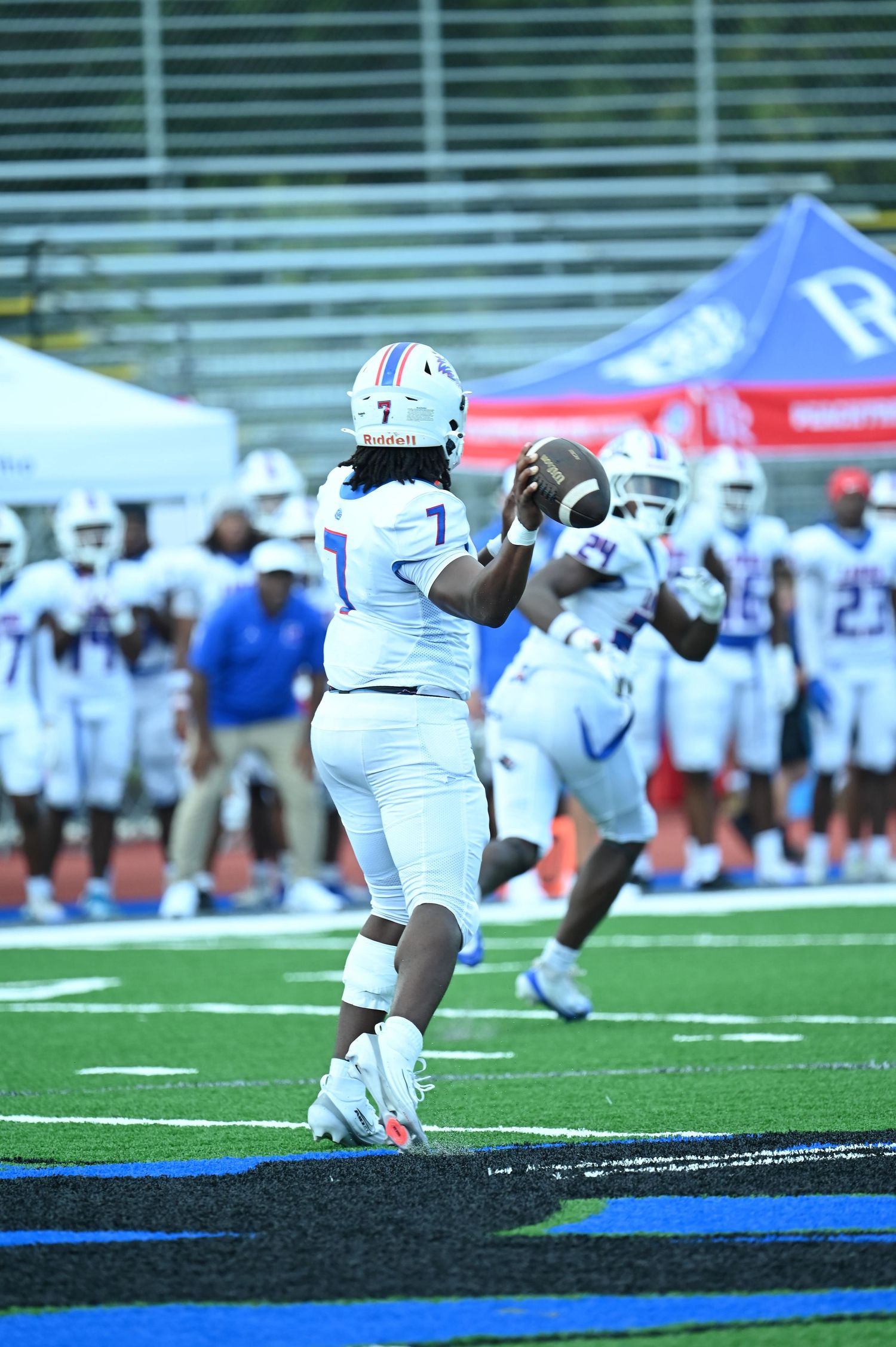 Football player wearing number 7 prepares to throw a pass during a college football game on a blue turf field.
