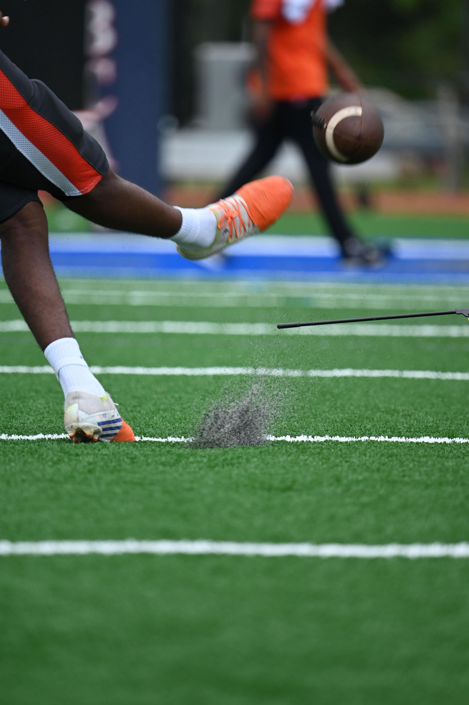 Football player kicking off the tee on a blue and green turf field during a game.