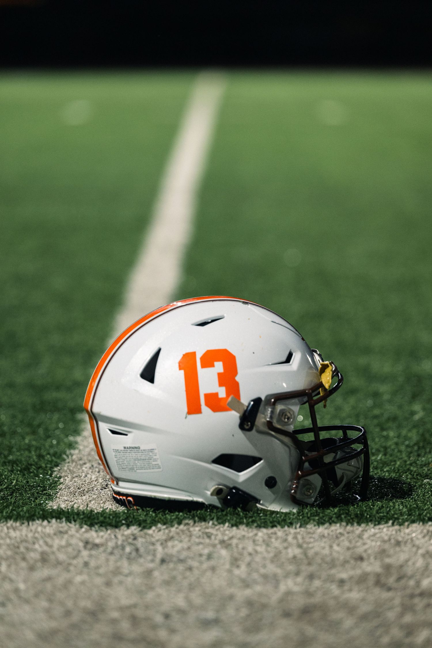White football helmet with number 13 and orange accents resting on green turf field.