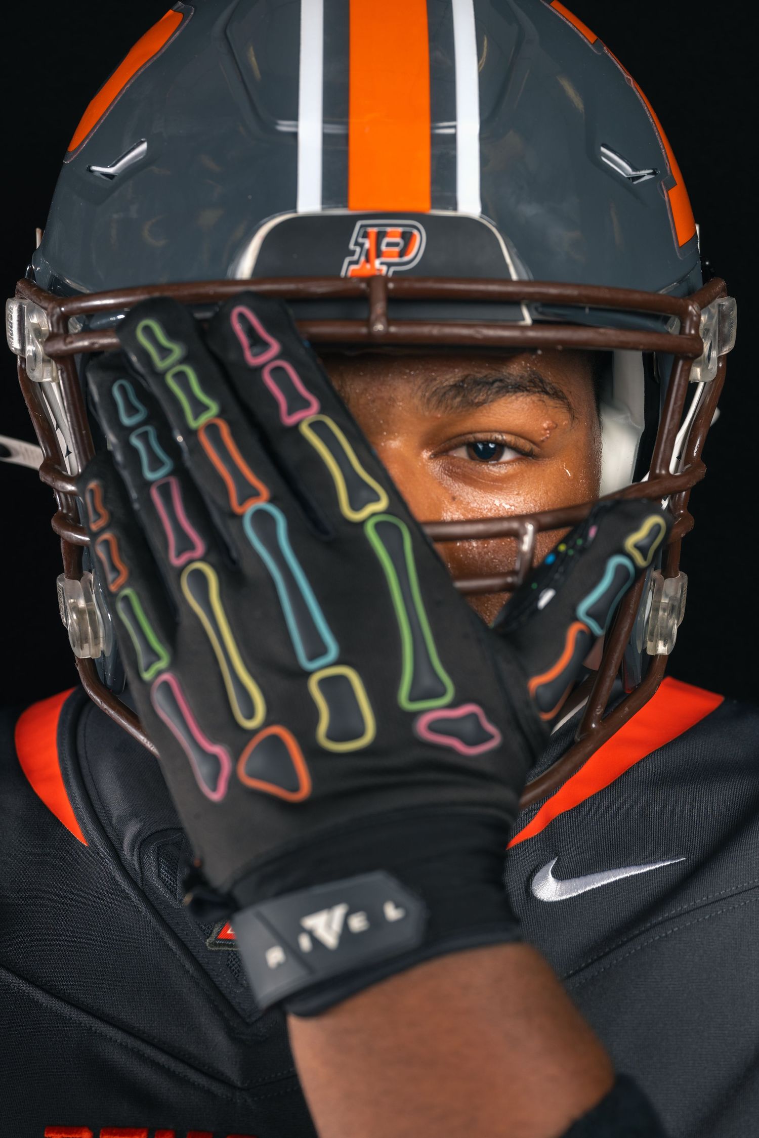 Close-up of football player in orange and black helmet with colorful skeleton-print Nike gloves covering face.