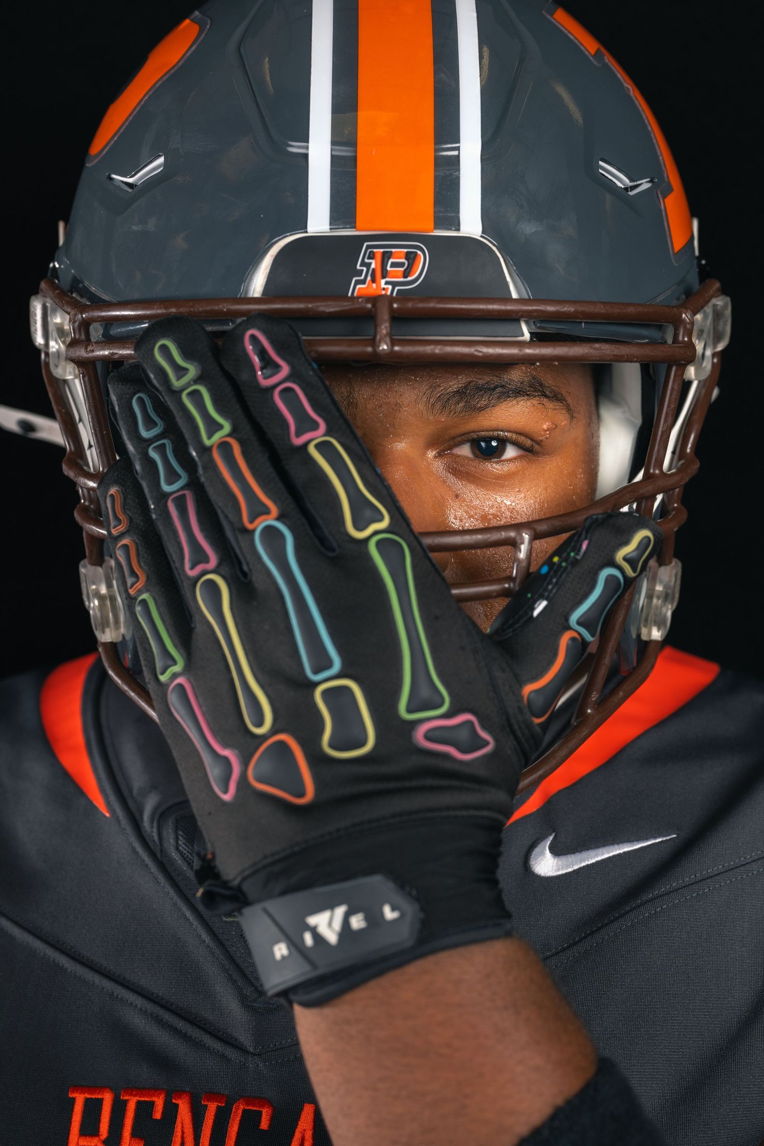 Piper Bengals football player in dark helmet holding skeleton glove over face in close-up portrait.