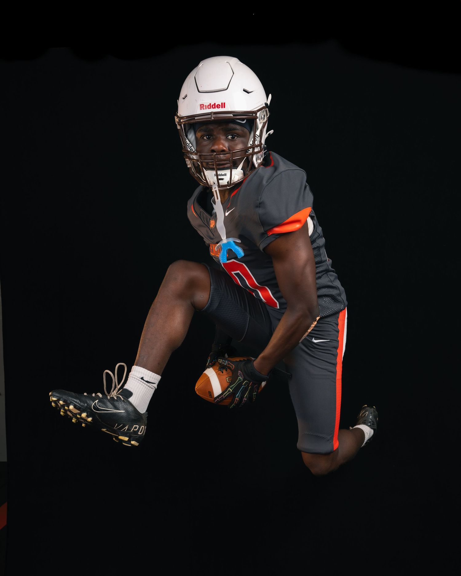 Bengals football player in gray Nike uniform leaping mid-air while catching ball against black background.