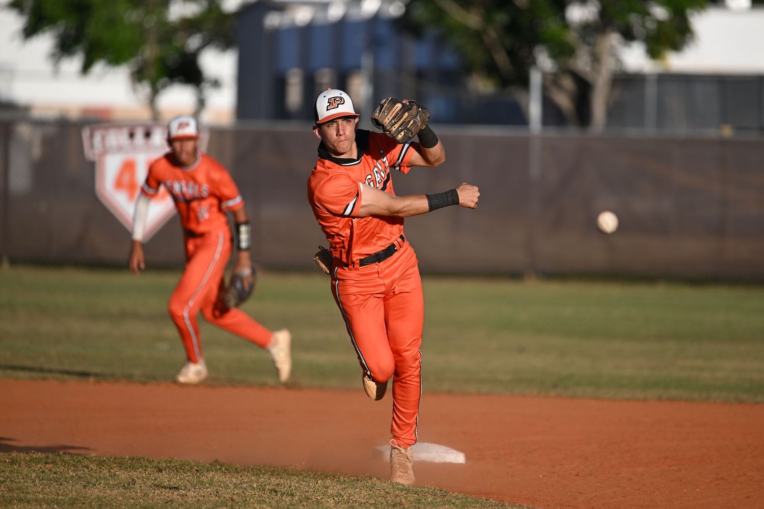 Baseball player in orange uniform throwing ball on field during a game.