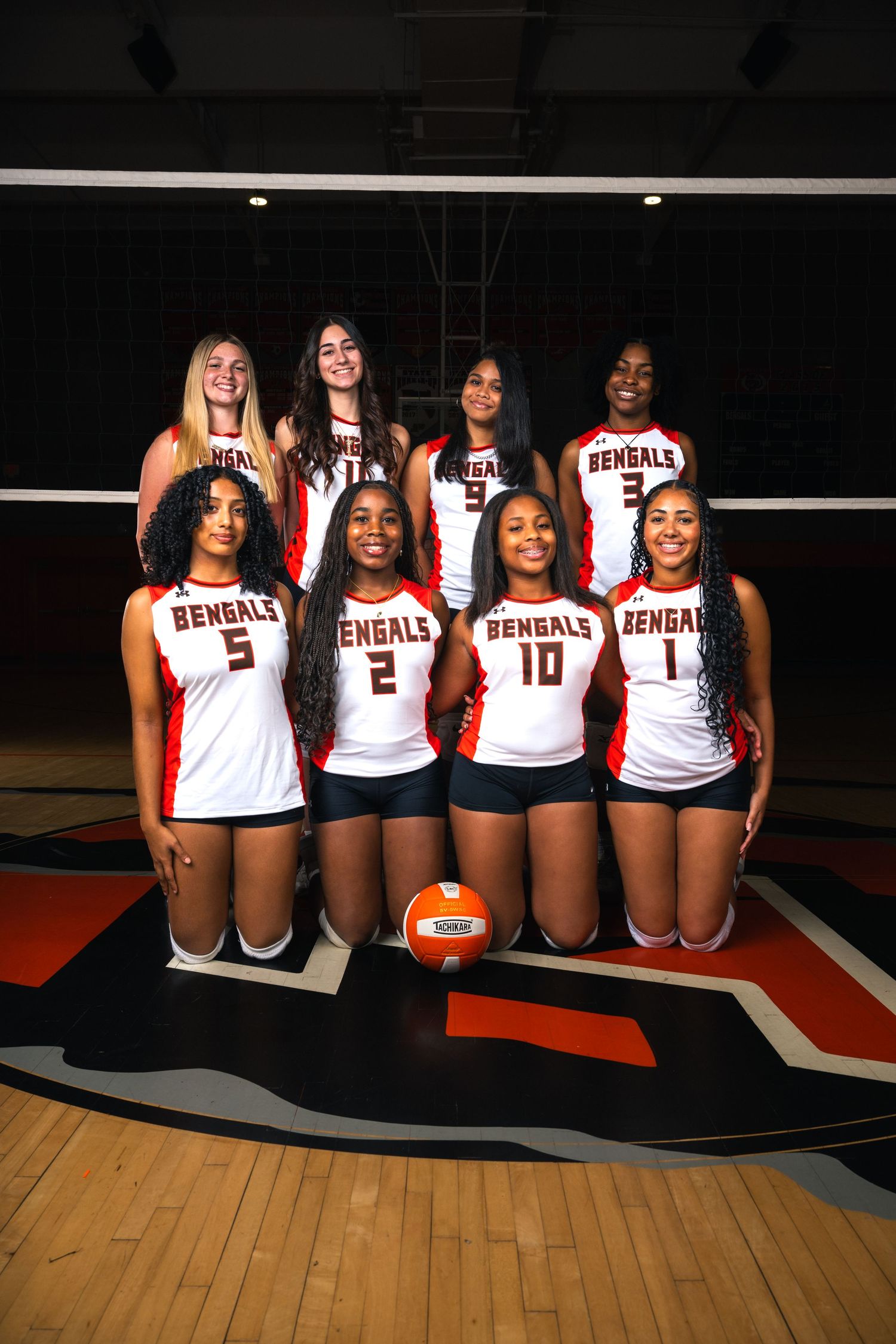 Bengals volleyball team poses for group photo on court, eight players in red and white uniforms with a volleyball.