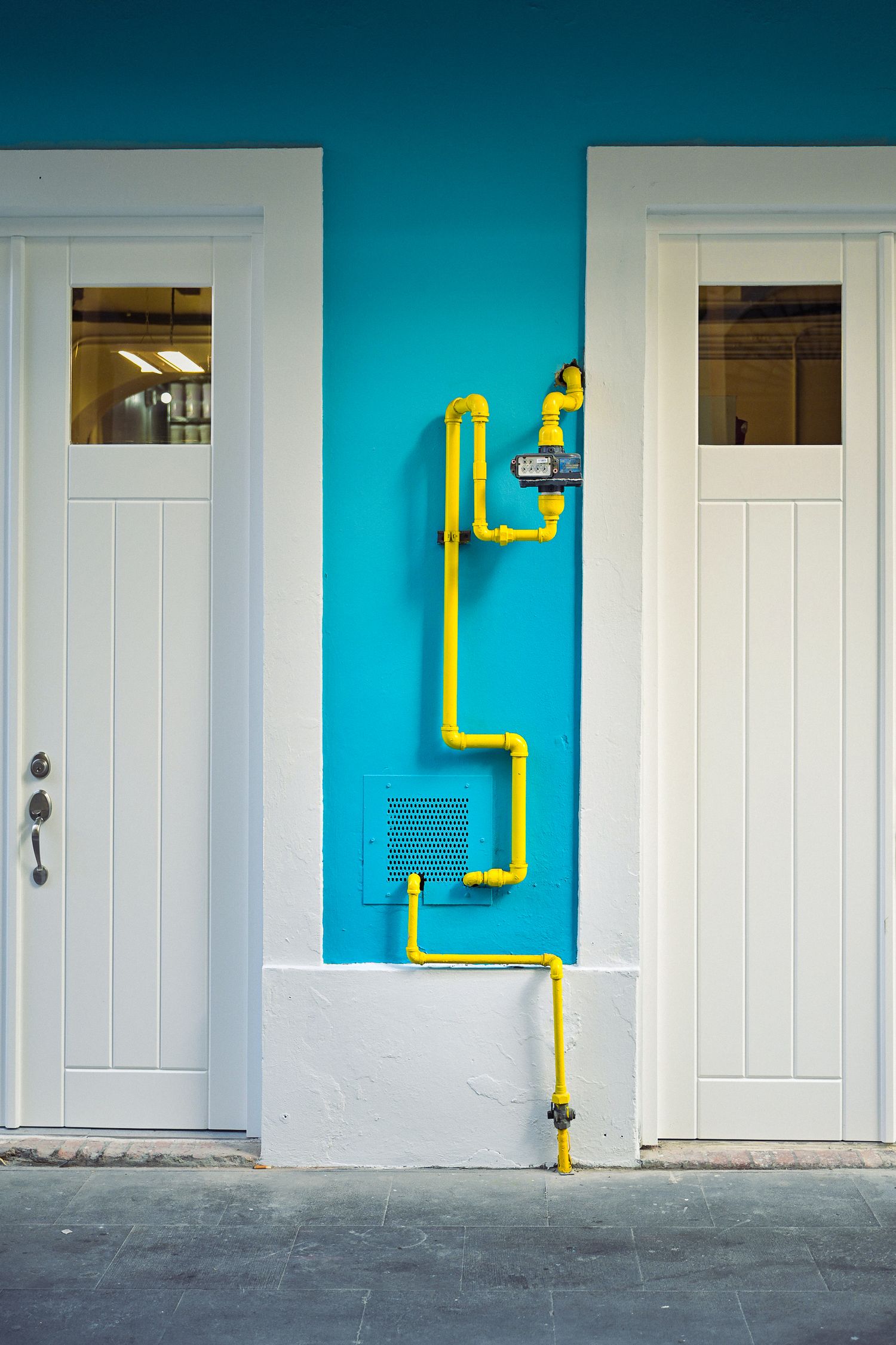 Yellow gas pipes on turquoise wall between two white doors on building exterior facade.