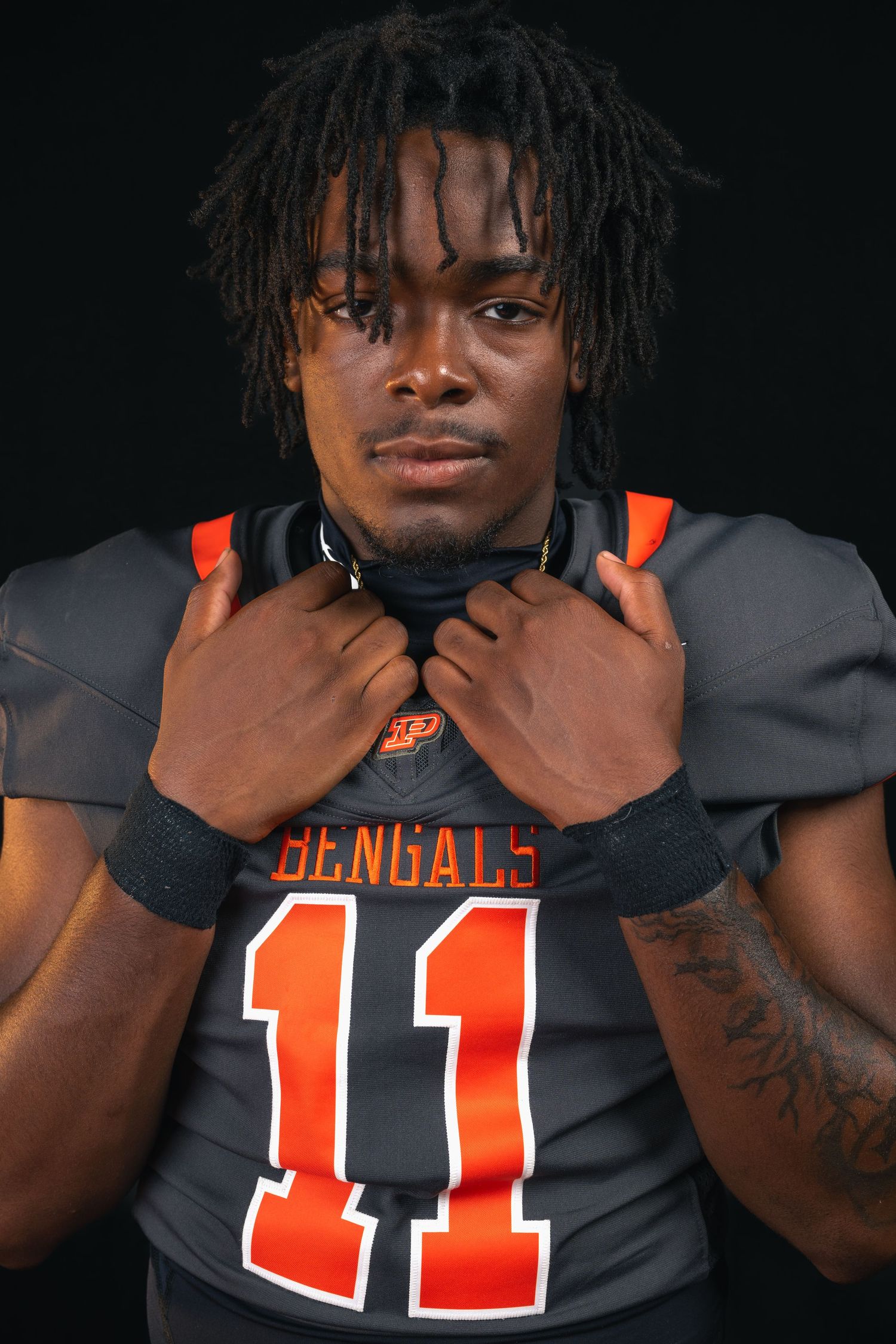 Bengals football player wearing jersey number 11 adjusting collar in dramatic portrait on black background.