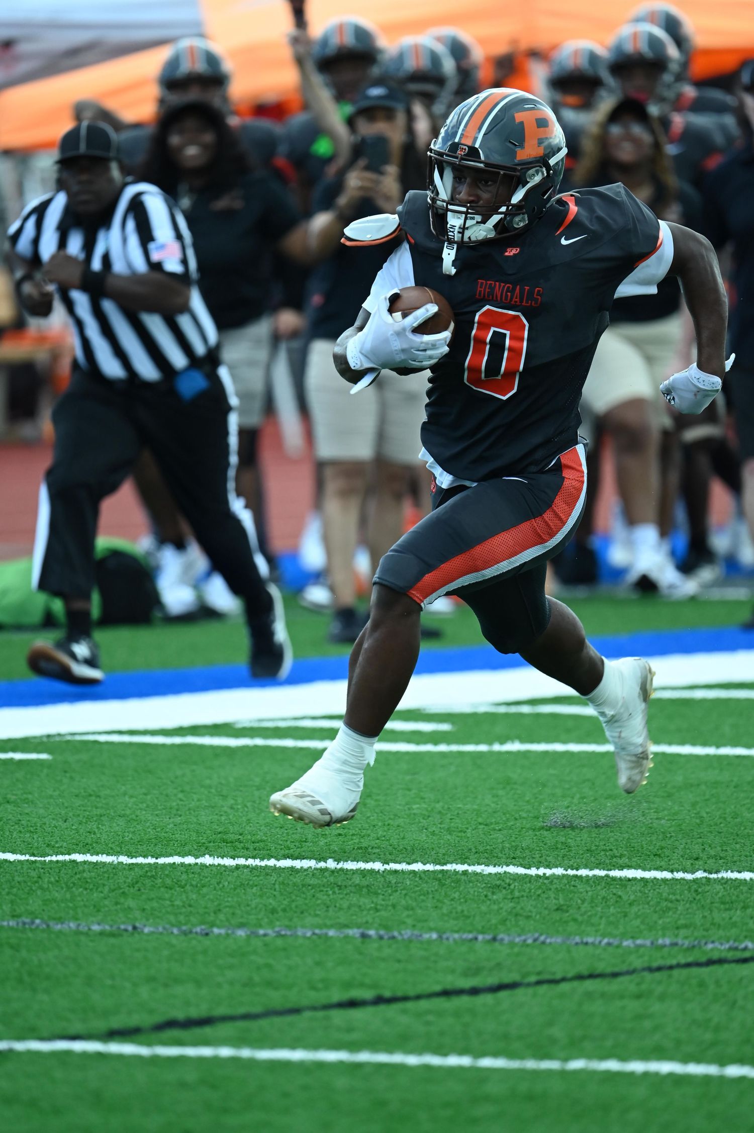 Football player wearing number 0 in black and orange Bengals uniform runs with the ball during a high school game.