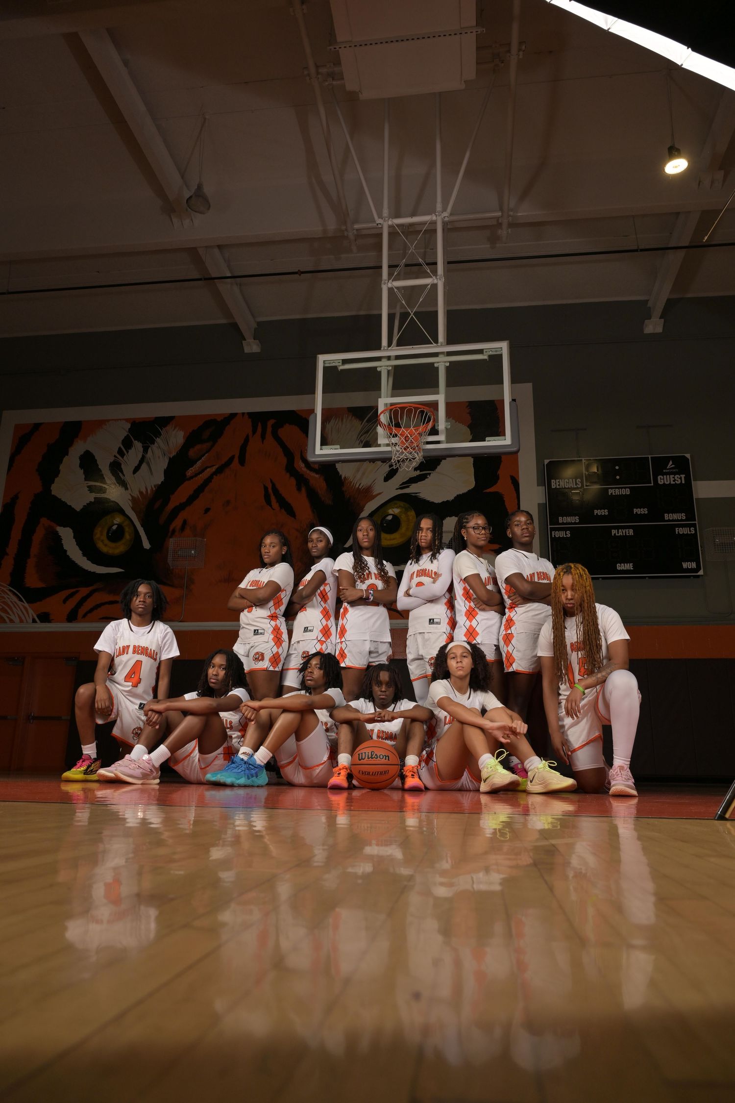 Women's basketball team poses together on a tiger-themed court in white uniforms for a team photo.