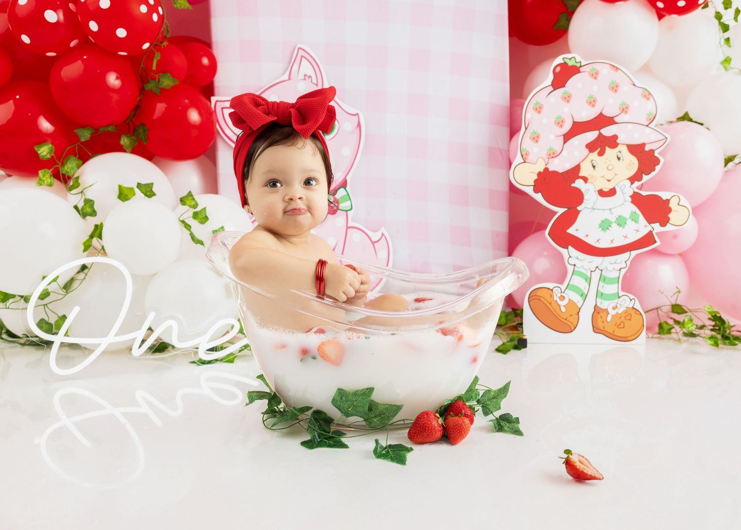 A sweet decorated bath setup with red strawberry theme decorations, white flowers, and pink accents.