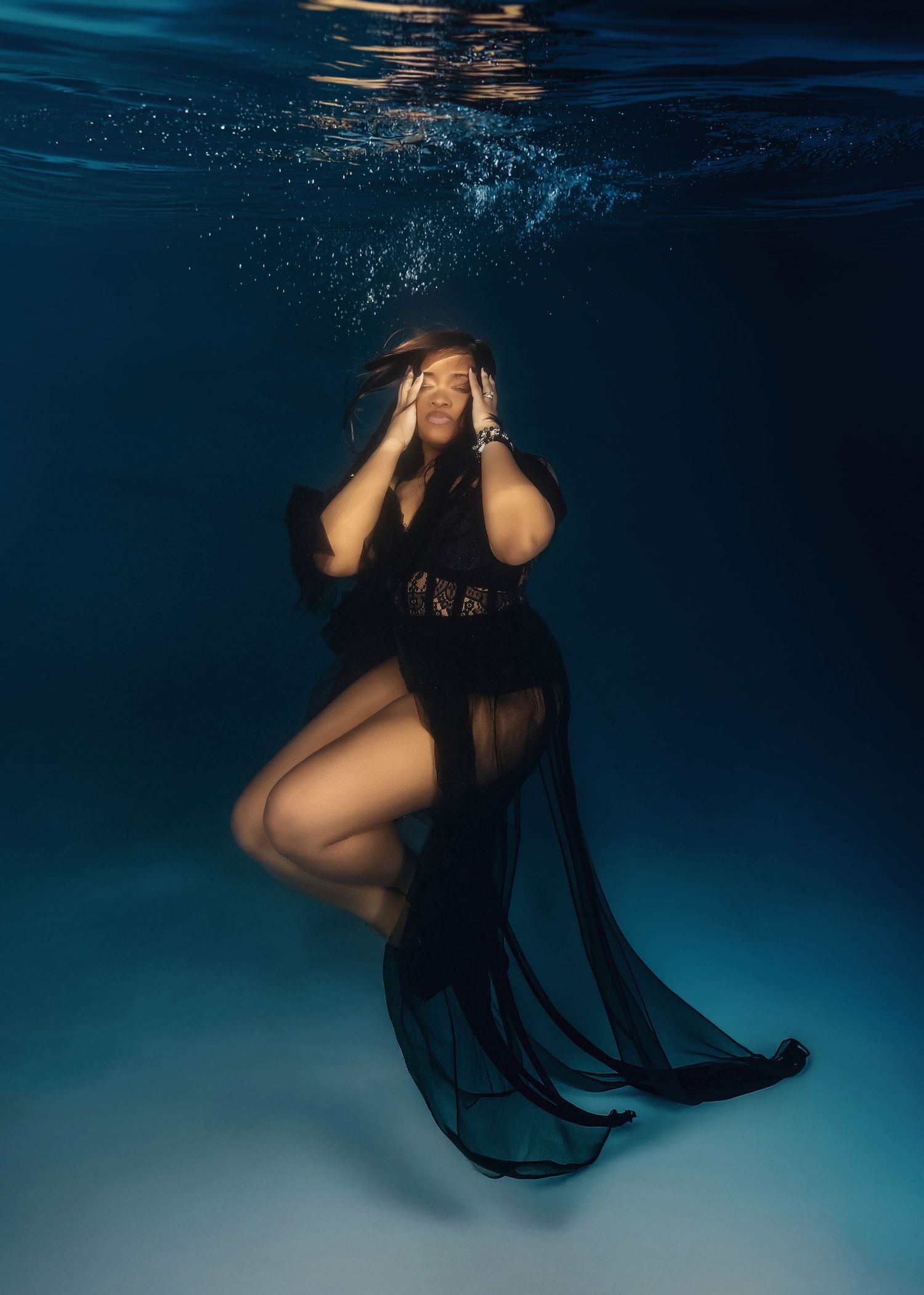 Artistic underwater photo series showing a figure in flowing black fabric moving gracefully through dark blue water.