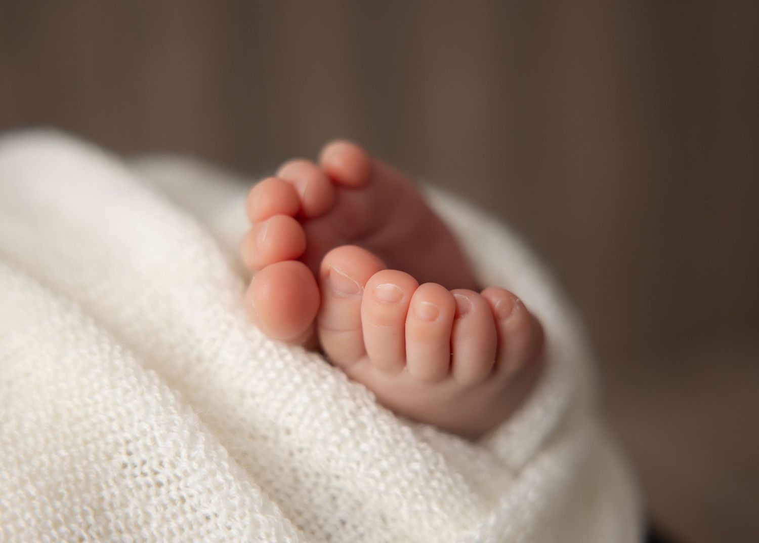 Close-up of tiny baby feet and toes resting on soft white blanket in natural lighting.