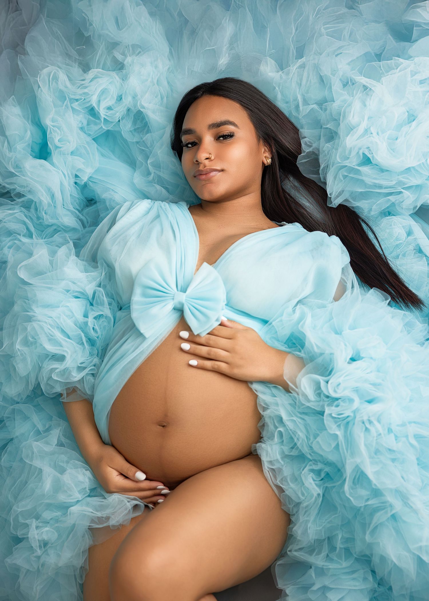 Artistic maternity photo series showing woman in ethereal light blue tulle dress against white background.