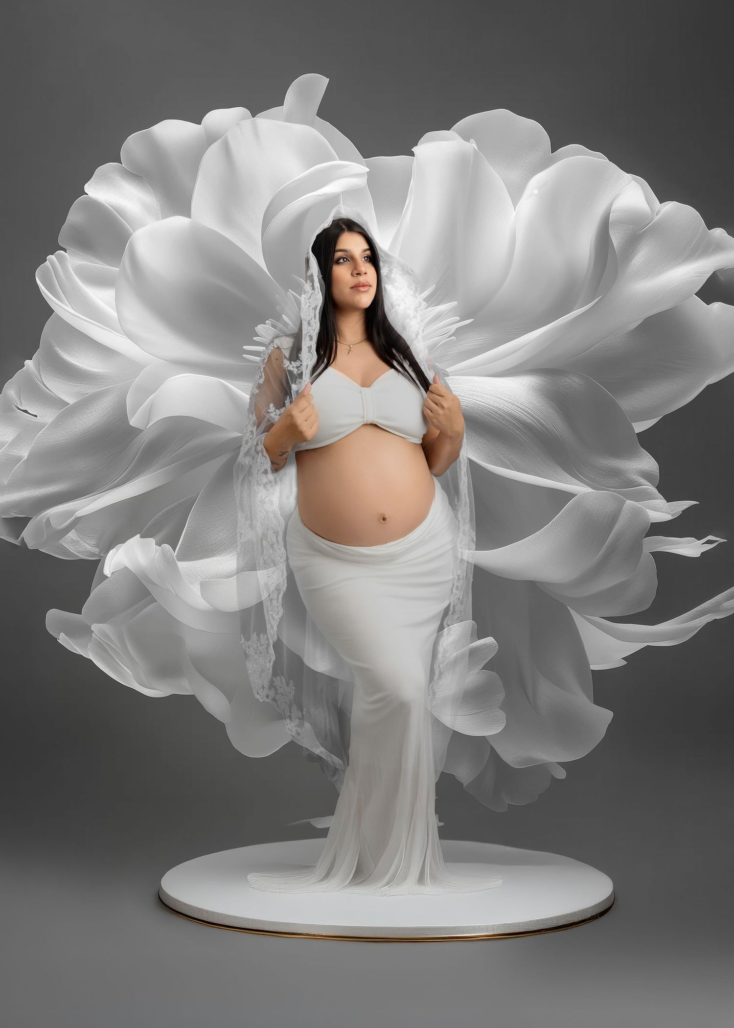 Artistic maternity photo featuring an ethereal white floral backdrop, flowing dress and sheer veil in dramatic lighting.