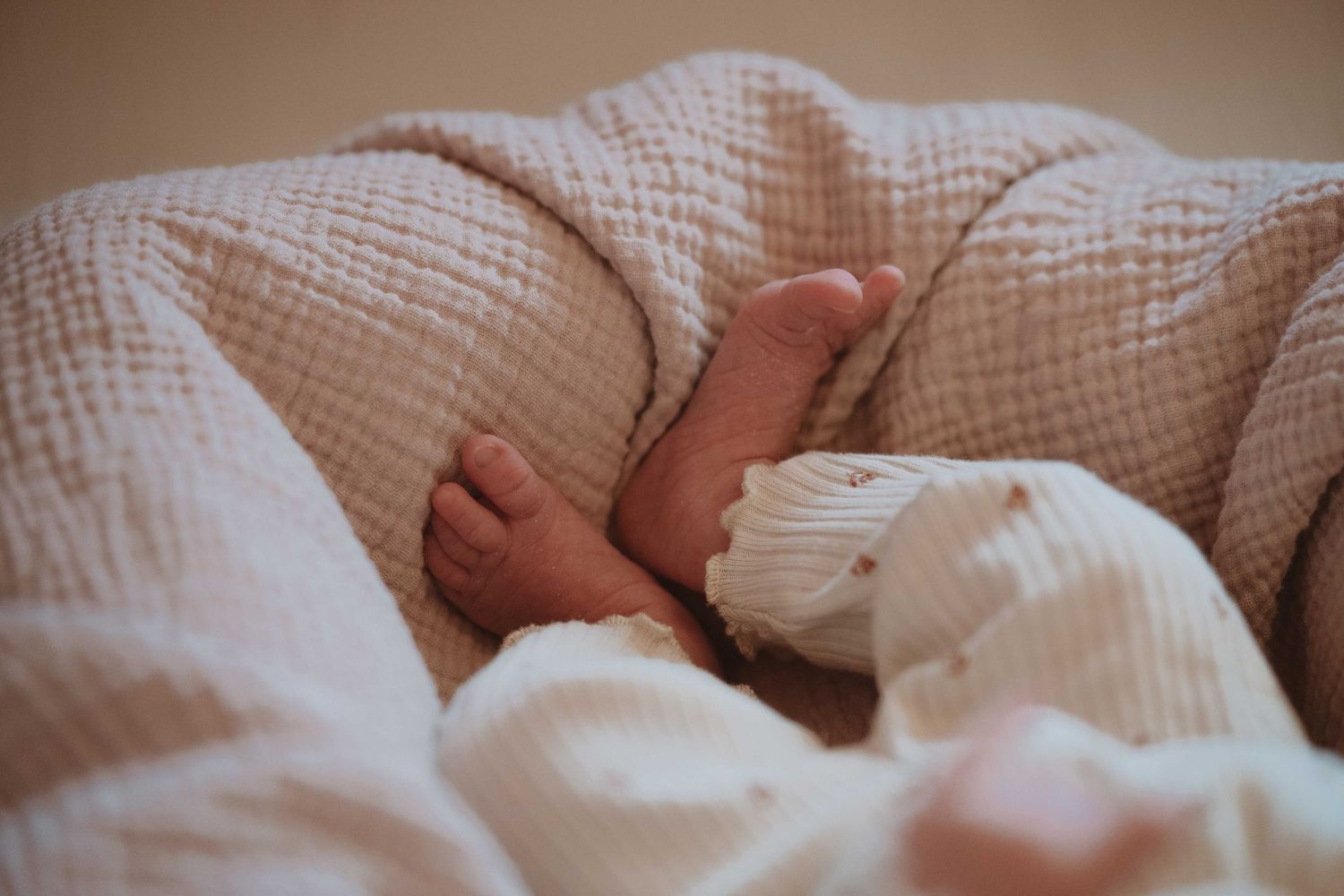 Close-up of a sleeping newborn baby's tiny feet tucked in soft white muslin blankets.