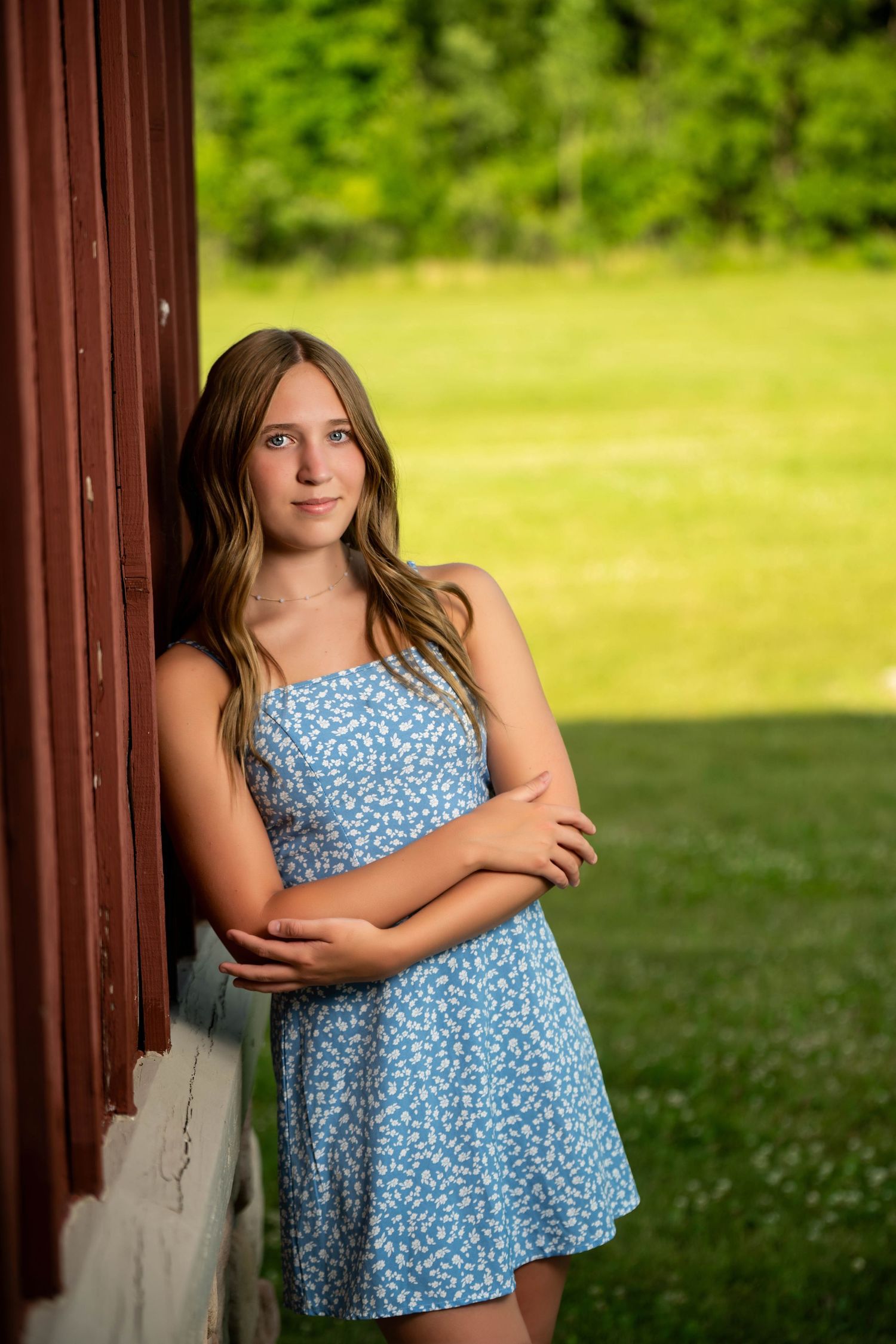 A young person in a blue floral dress poses against a rustic brown column outdoors.