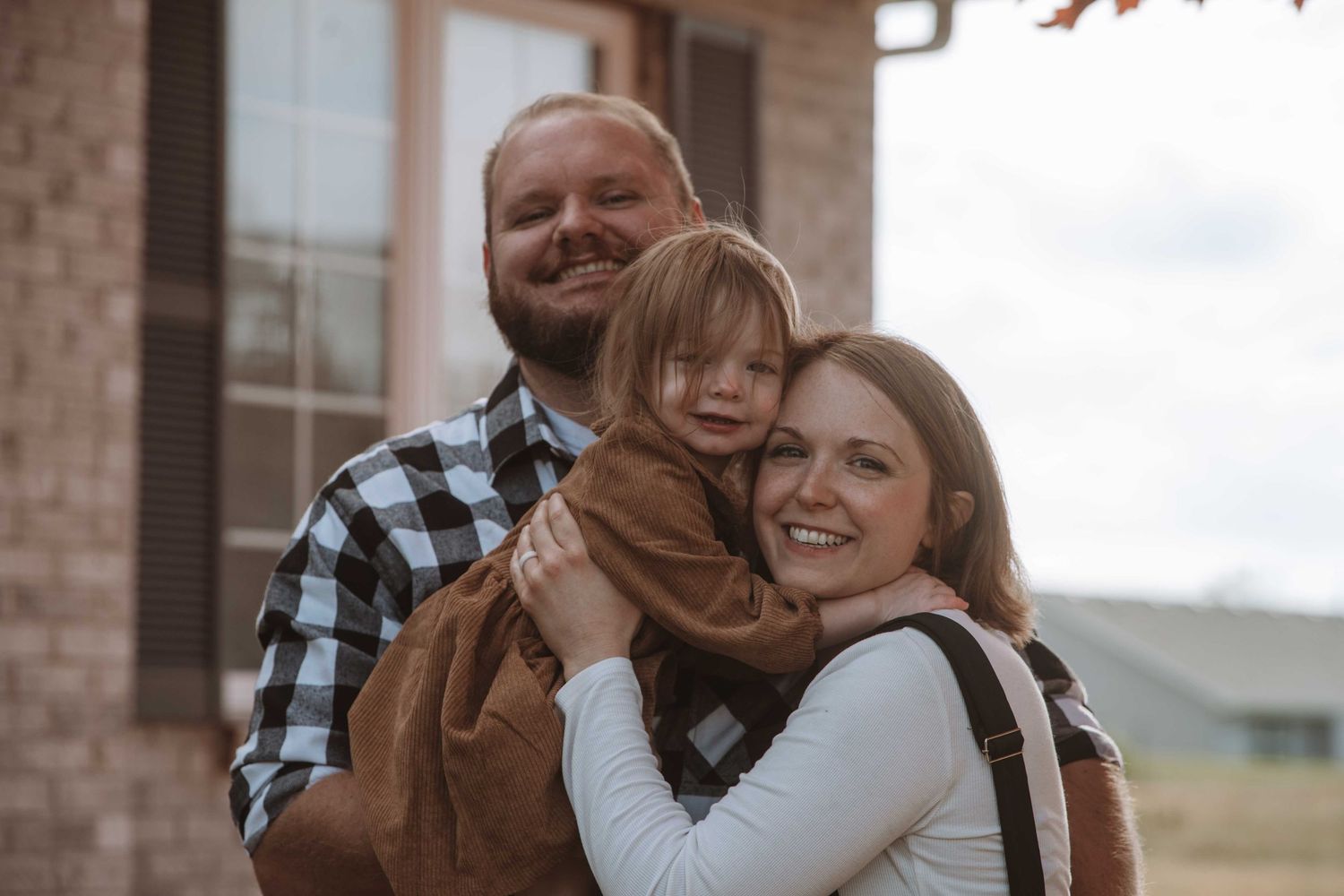 A couple shares joyful moments together outdoors against a brick wall background in a casual photo session.