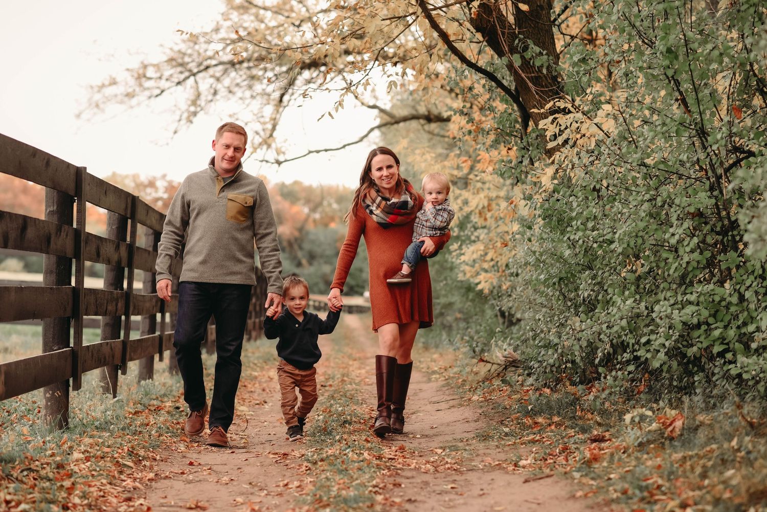 People walking together on a scenic fall path with golden leaves and wooden fencing.