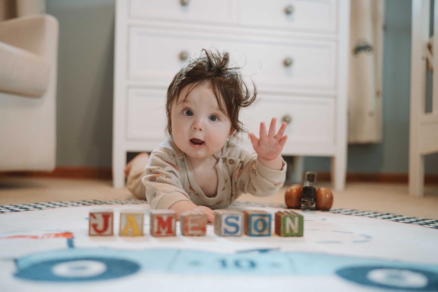 Baby boy lying on a play mat with colorful alphabet blocks spelling JAMESON in a bright nursery room.
