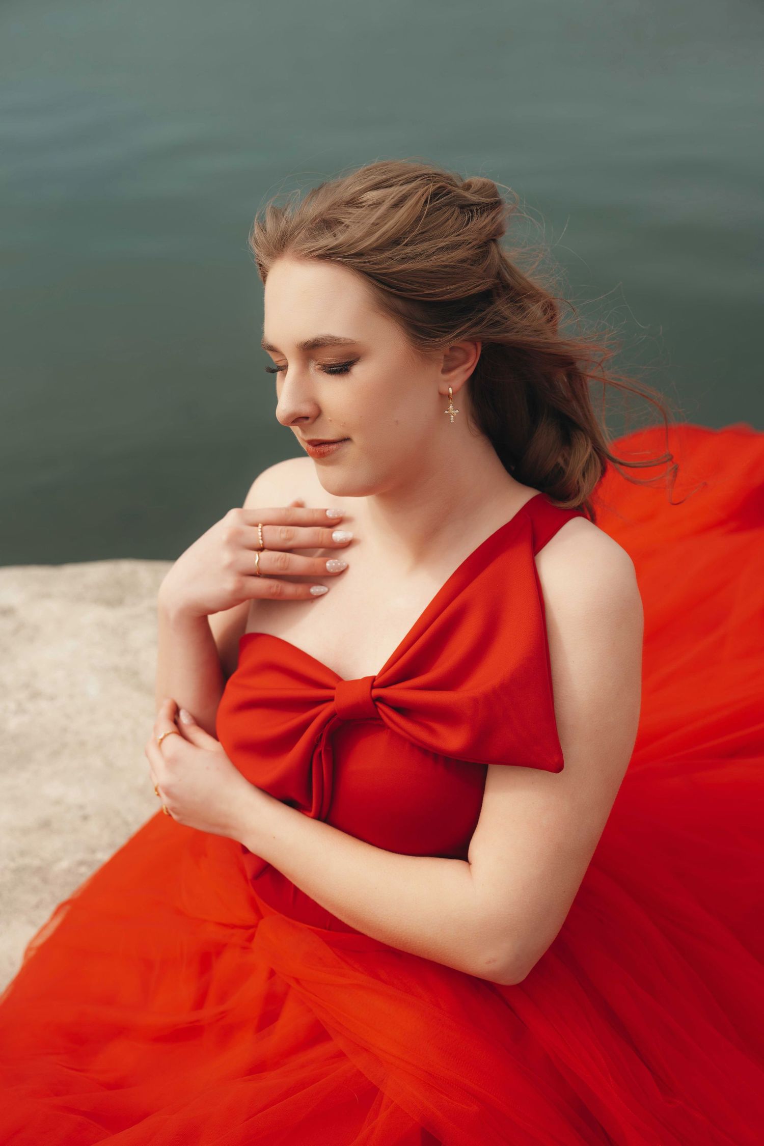 A woman in a flowing red dress poses artistically against a dark water backdrop in a series of connected photos.