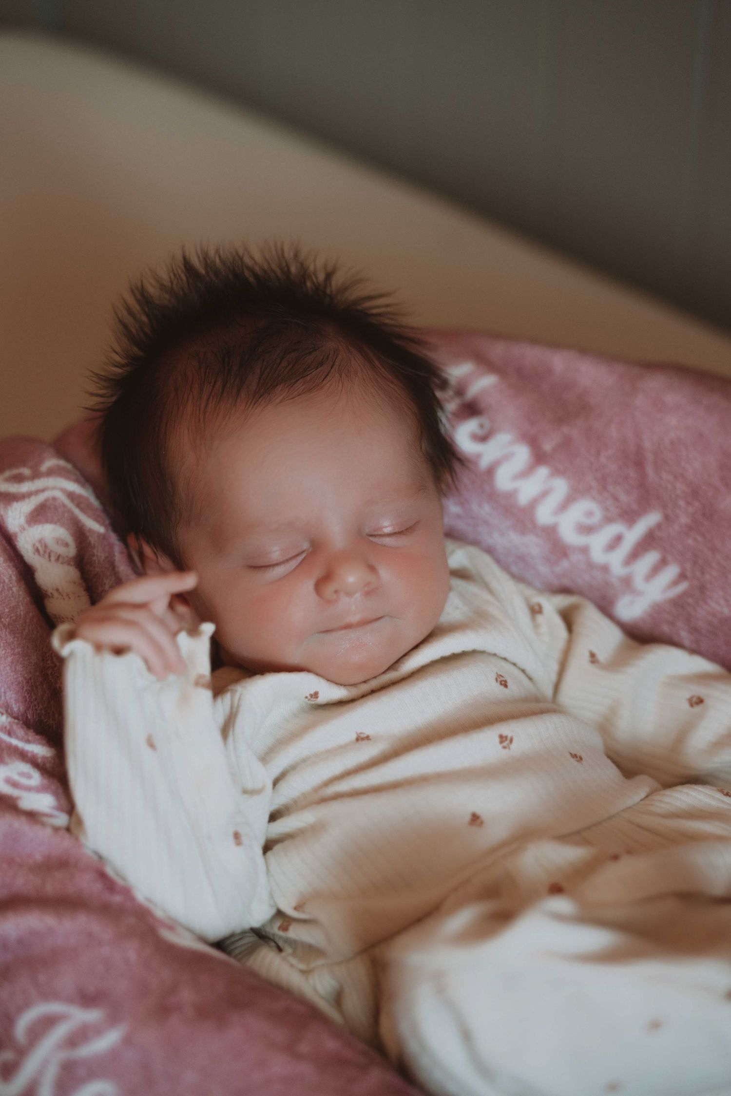 Newborn baby named Kennedy sleeping peacefully on a pink blanket, wearing a white onesie with tiny heart details.