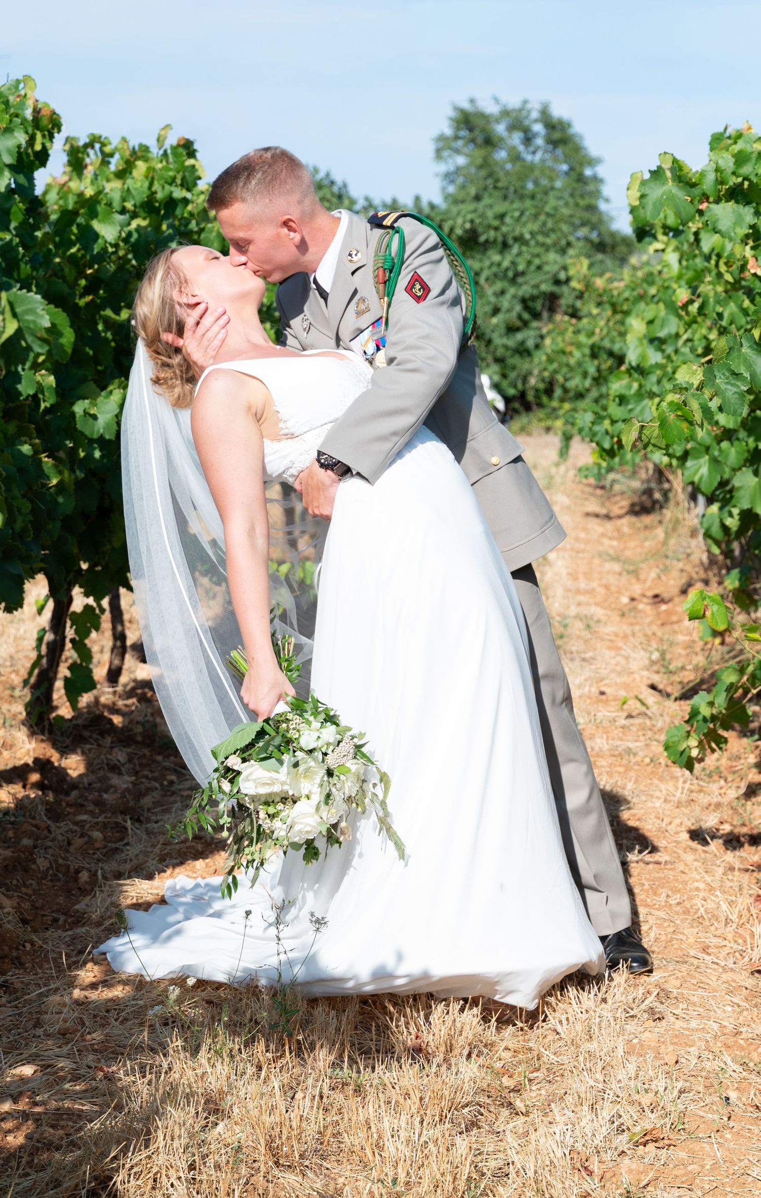 Wedding couple posing in vineyard with flowing white dress and military uniform.