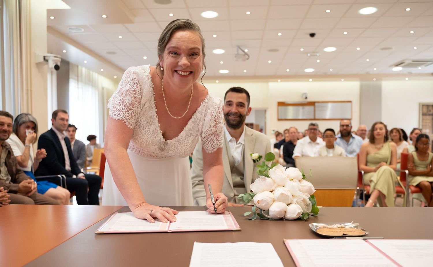 Person in white lace dress signing marriage documents at ceremony.