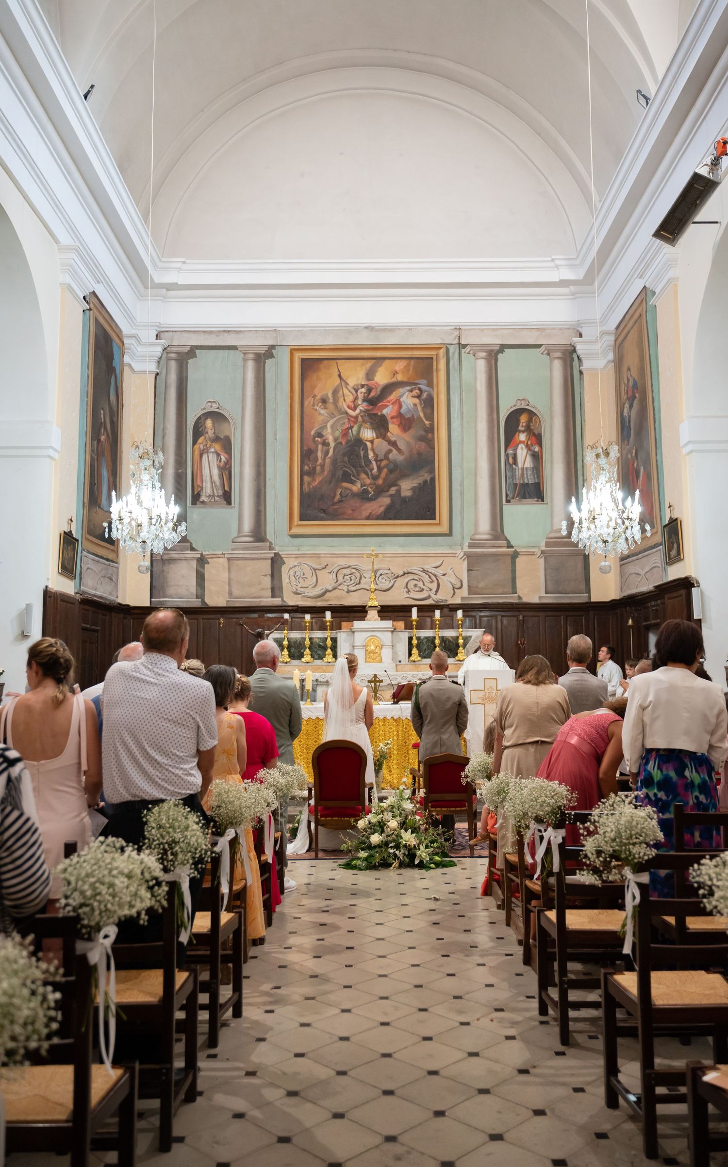 Interior of historic church with religious artwork and chandeliers during wedding ceremony.