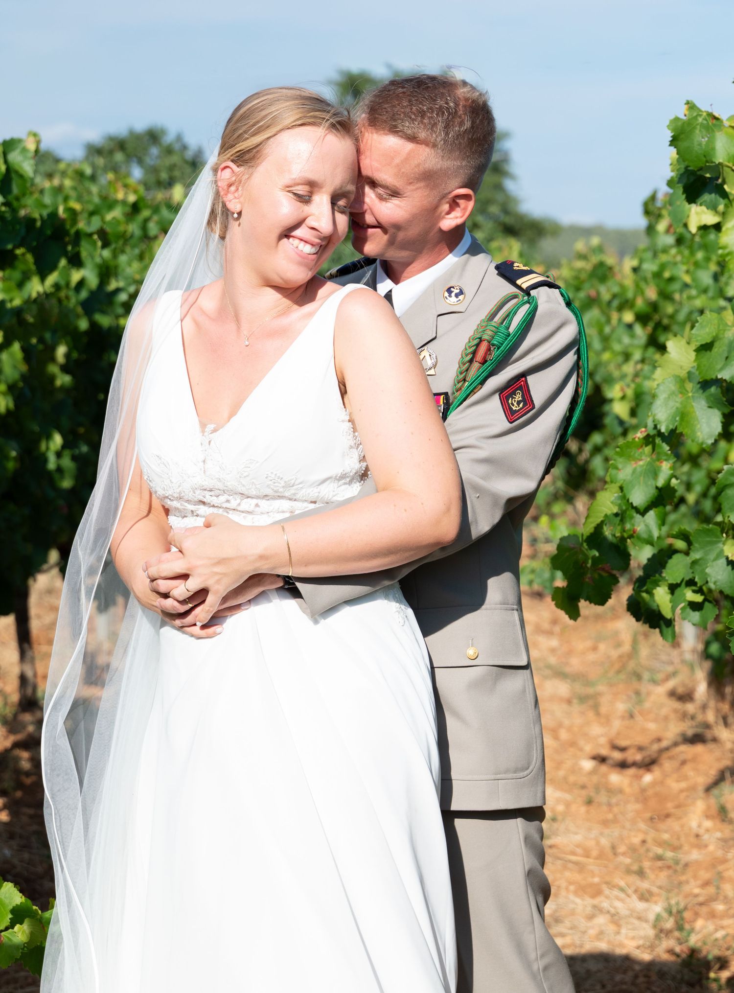 Newlyweds sharing intimate moment among grapevines in sunlit vineyard.