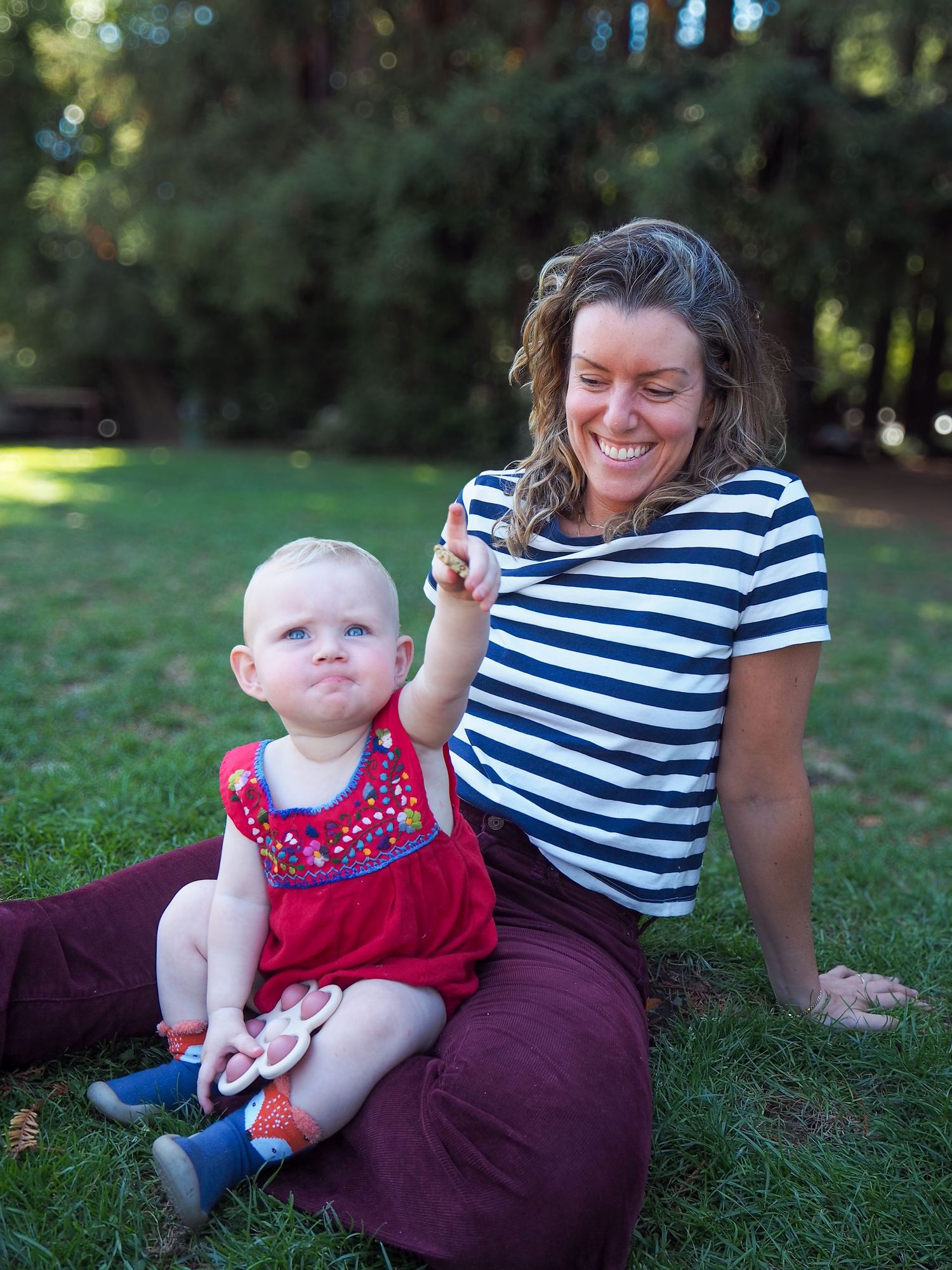 An outdoor summer scene with striped shirt and burgundy pants while sitting on grass.