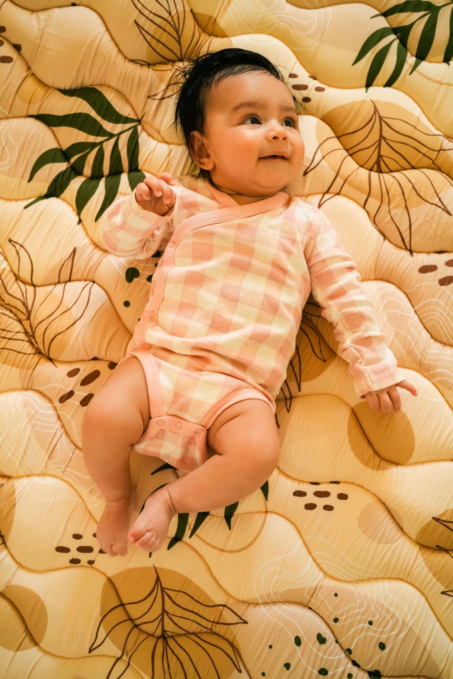 Small infant lying on patterned bedding in peachy pink outfit.