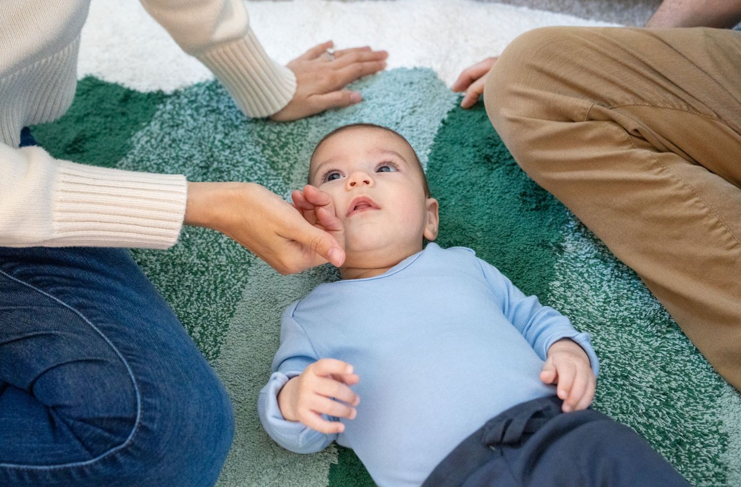 A sequence of photos showing a baby receiving a massage on a green carpet.