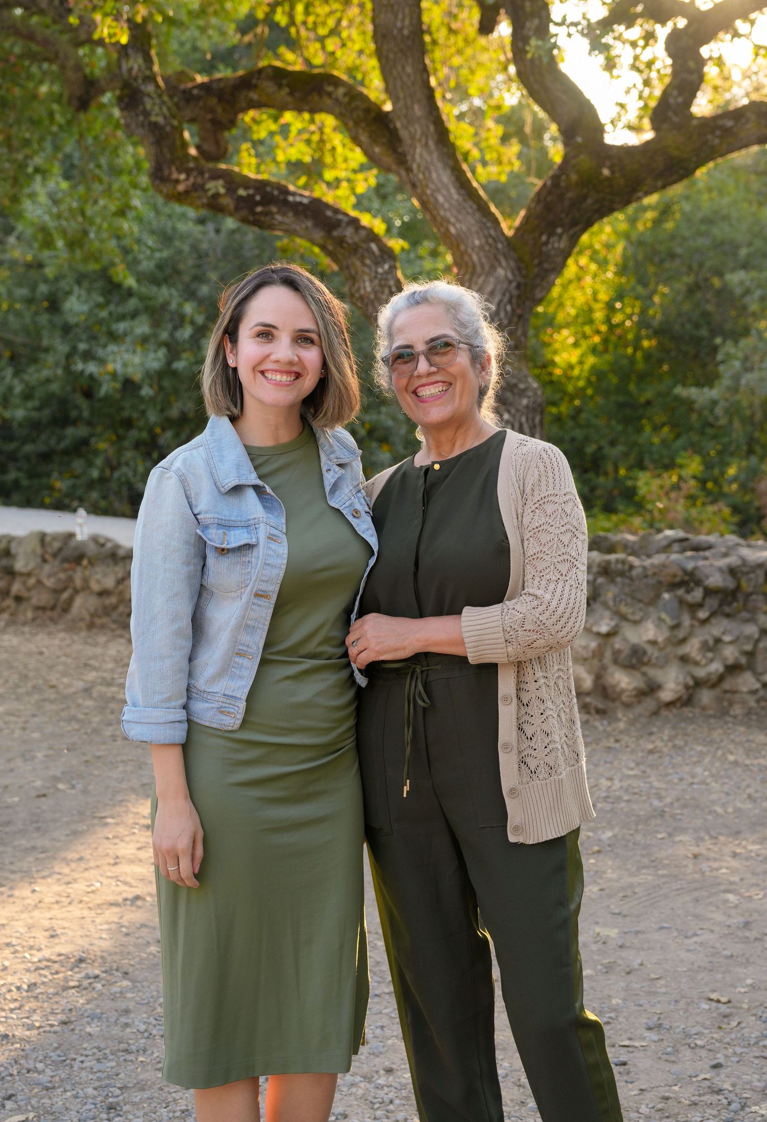 Two people stand close together wearing coordinating outfits against a natural outdoor backdrop.