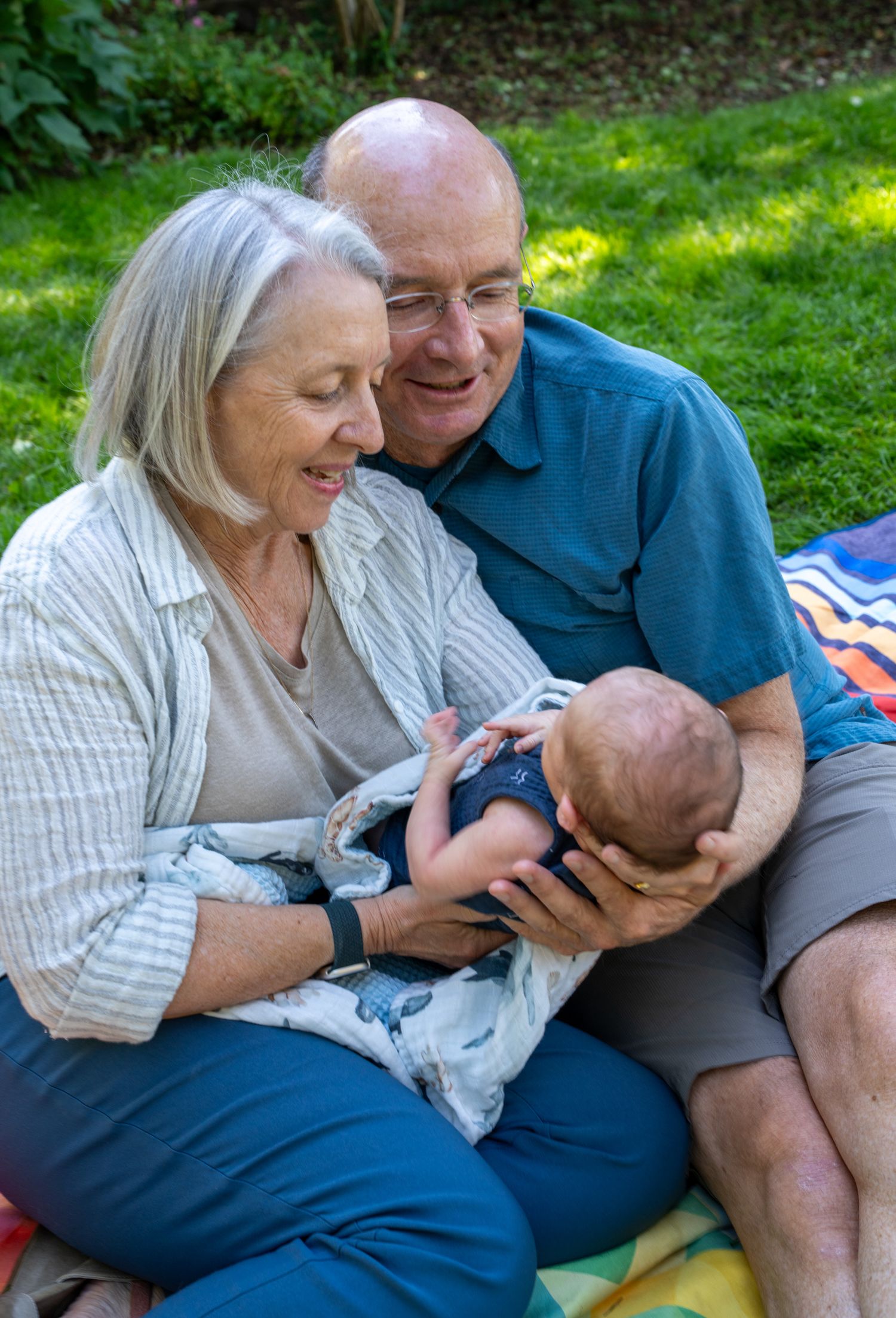 Loving couple sharing tender moments with their infant while relaxing outdoors on a sunny day.