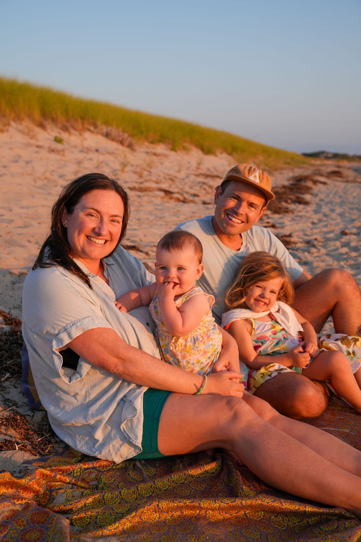 A family relaxes together on a sandy beach during golden hour sunset.