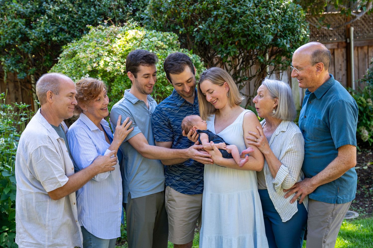 Multi-generational family gathering outdoors in a garden looking down at something together with joy.